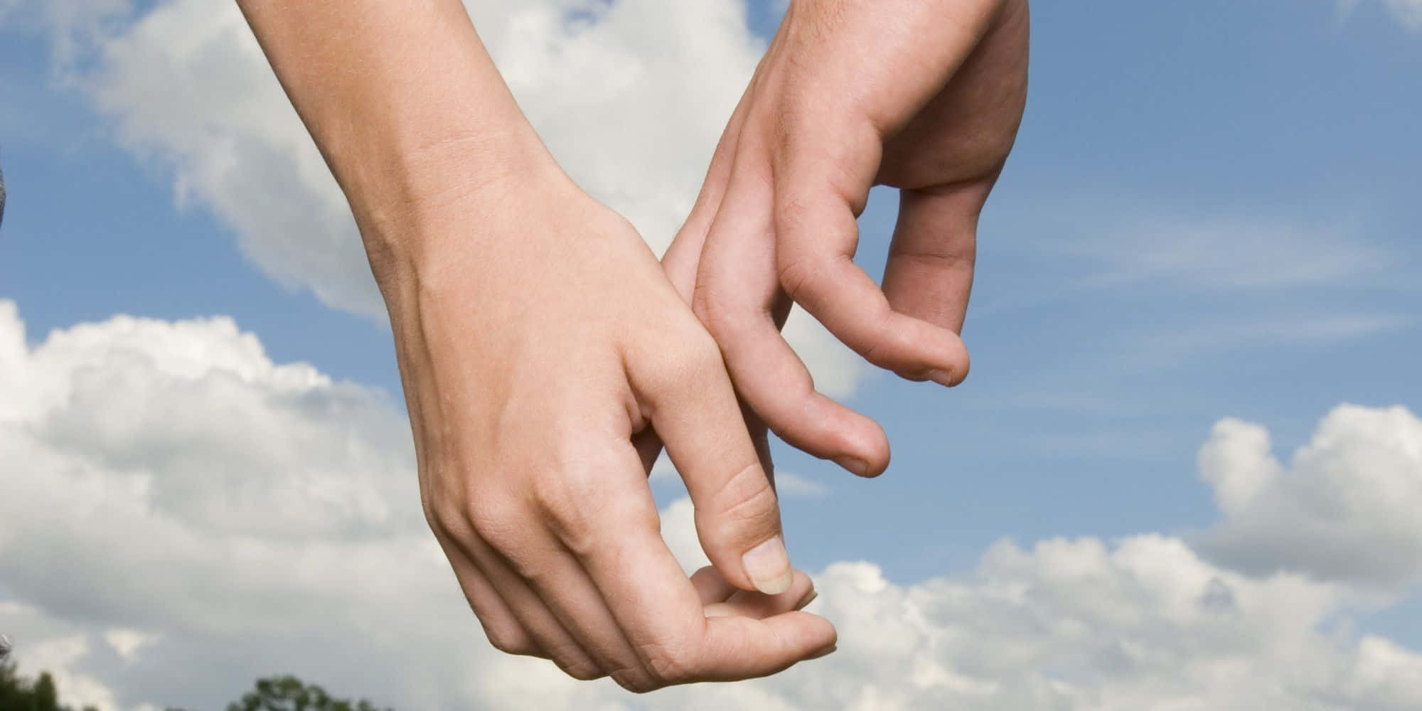 Holding Hands 桌布 壁紙 — 兩隻手輕輕交握，背景是明亮的藍天和蓬鬆的白雲。