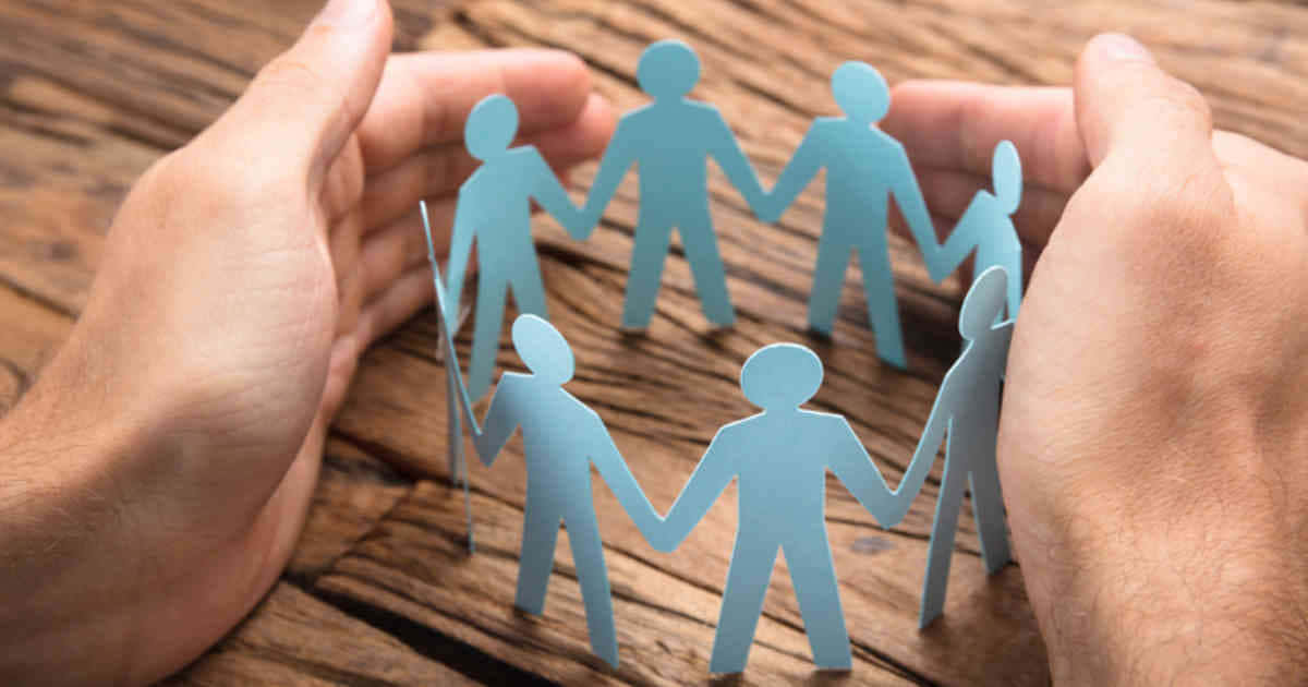 Inclusive 桌布 壁紙 — 兩隻手輕輕托住一個由淺藍色紙人組成的圓圈，紙人們在質樸的木質表面上手牽手。
