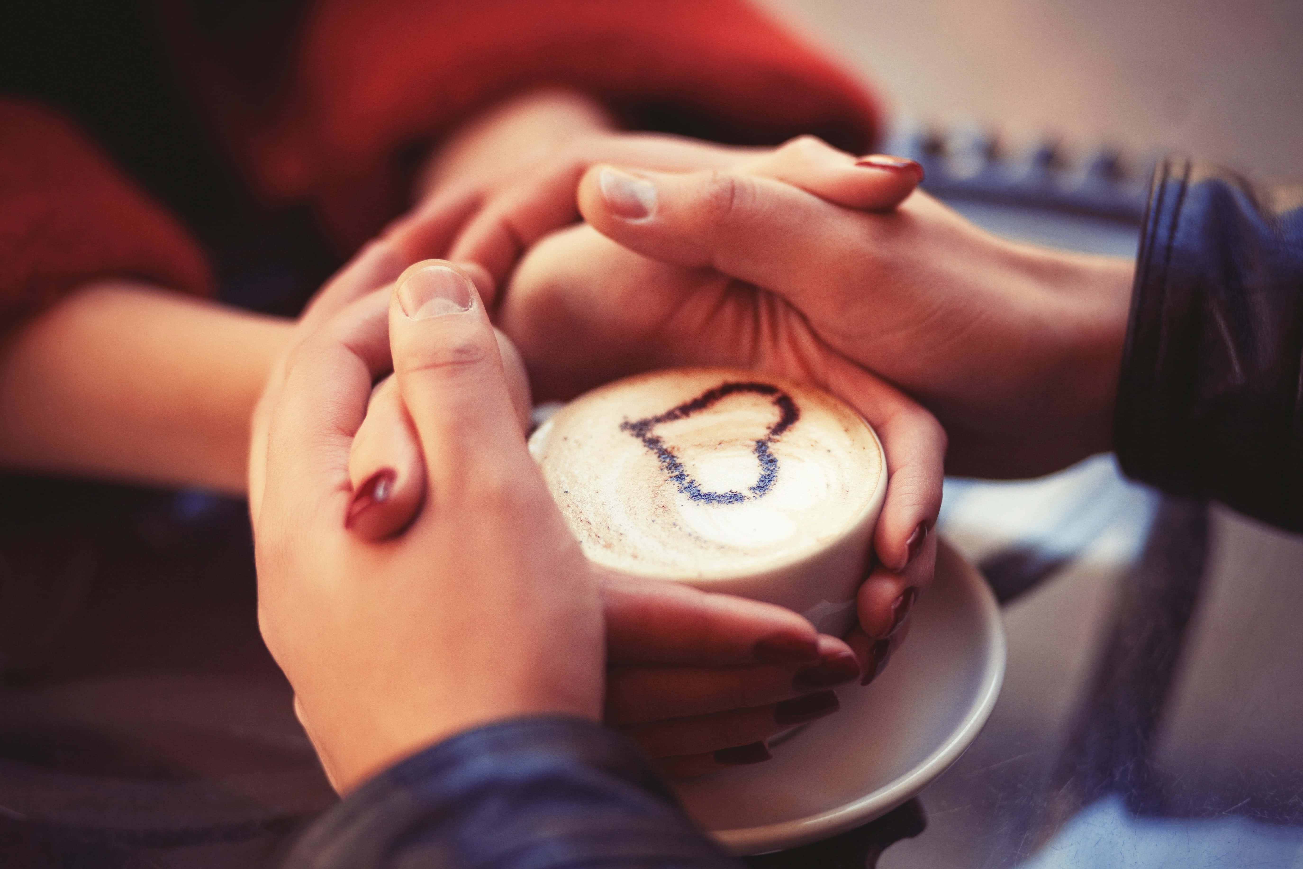 Couple Holding Hand 桌布 壁紙 — 兩隻手輕輕捧著一個帶有心形拉花圖案的咖啡杯，在溫暖親密的燈光下。