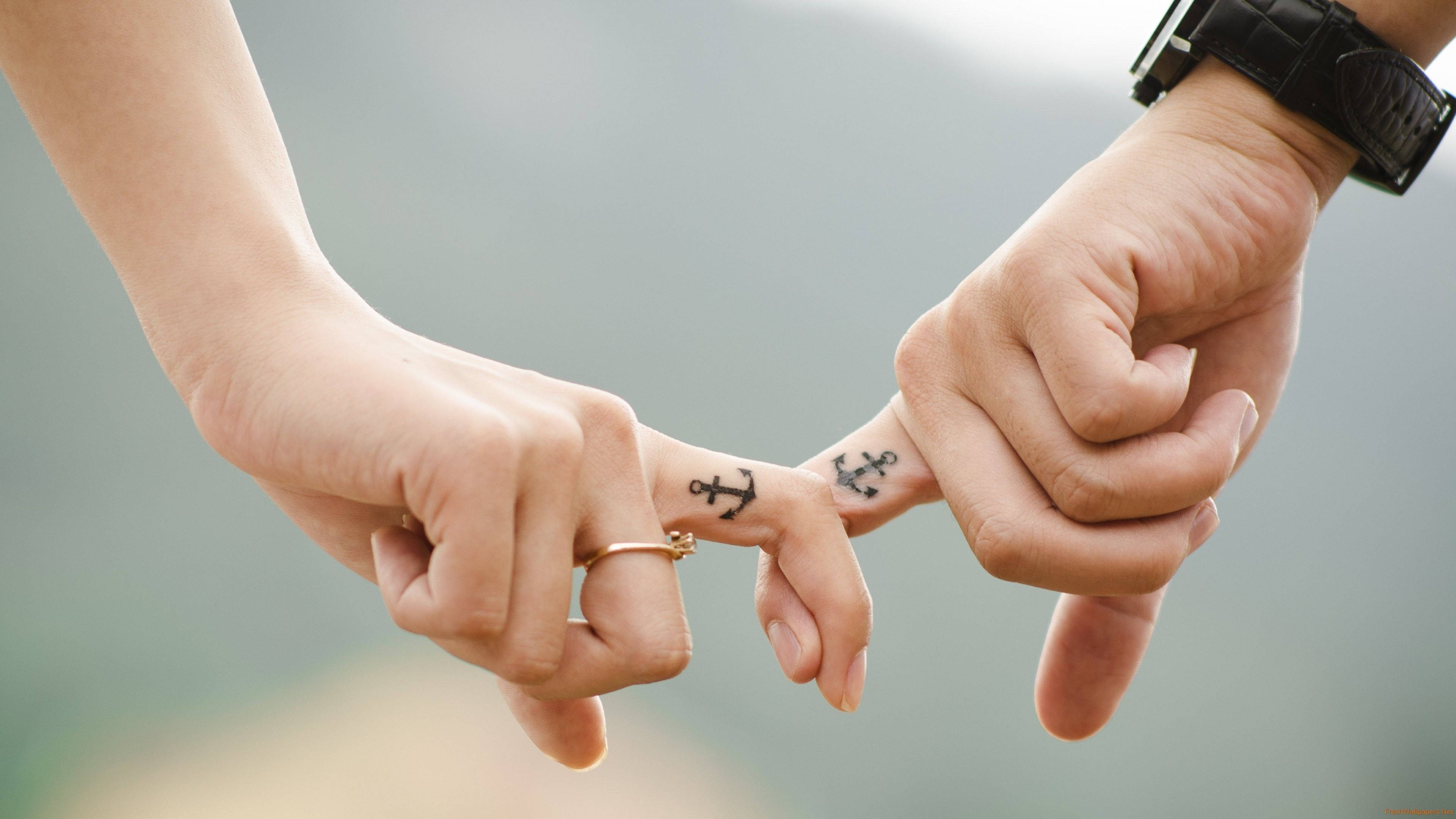Love Story 桌布 壁紙 — 兩隻手輕輕觸碰指尖，露出相配的錨紋身，象徵著在柔和模糊背景下的持久愛情。