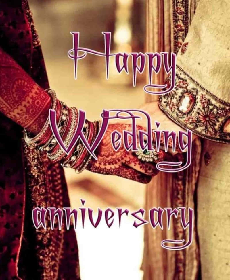 Anniversary 桌布 壁紙 — 兩隻手飾有指甲花和手鐲，緊握在一起，背景溫暖模糊，帶有「Happy Wedding Anniversary」文字的特寫。