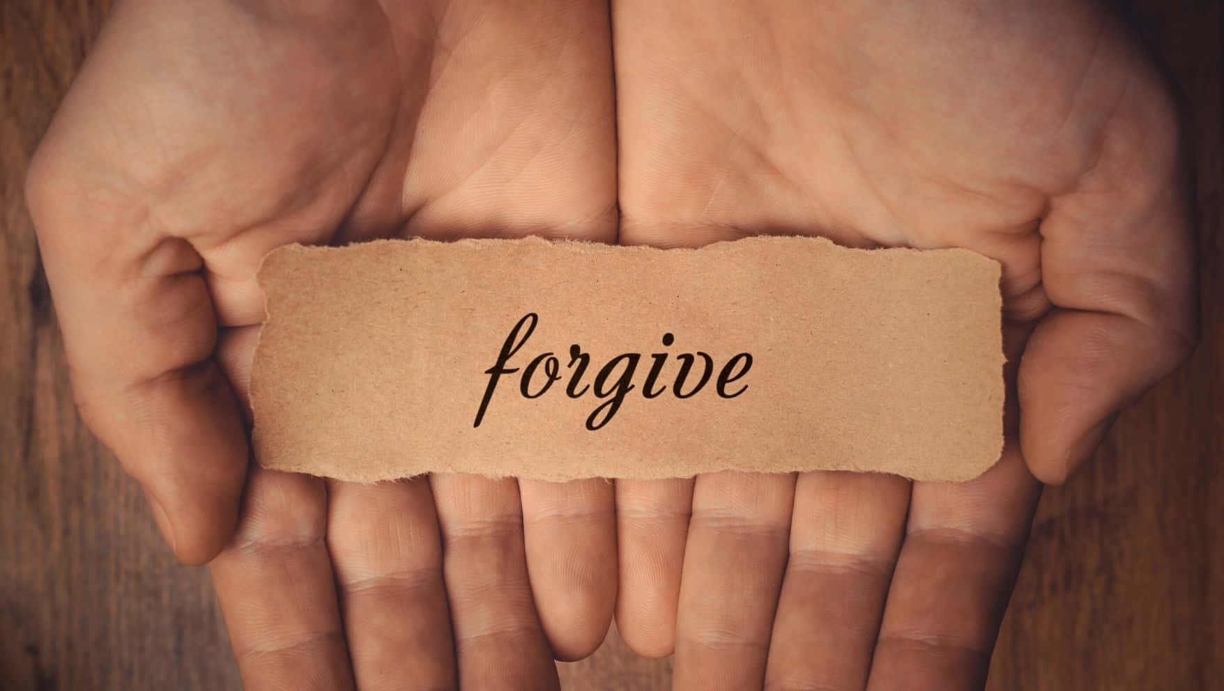 forgive 桌布 壁紙 — 兩隻捧著的手輕輕托著一條撕破的棕色紙條，上面以優雅的黑色草書寫著原諒二字。