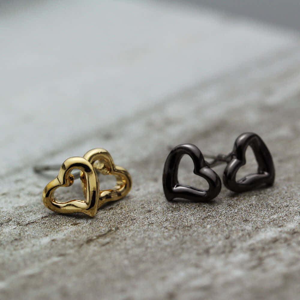 Cute Love 桌布 壁紙 — 兩隻極簡心形耳環金色和黑色放在有紋理的灰色石面上。