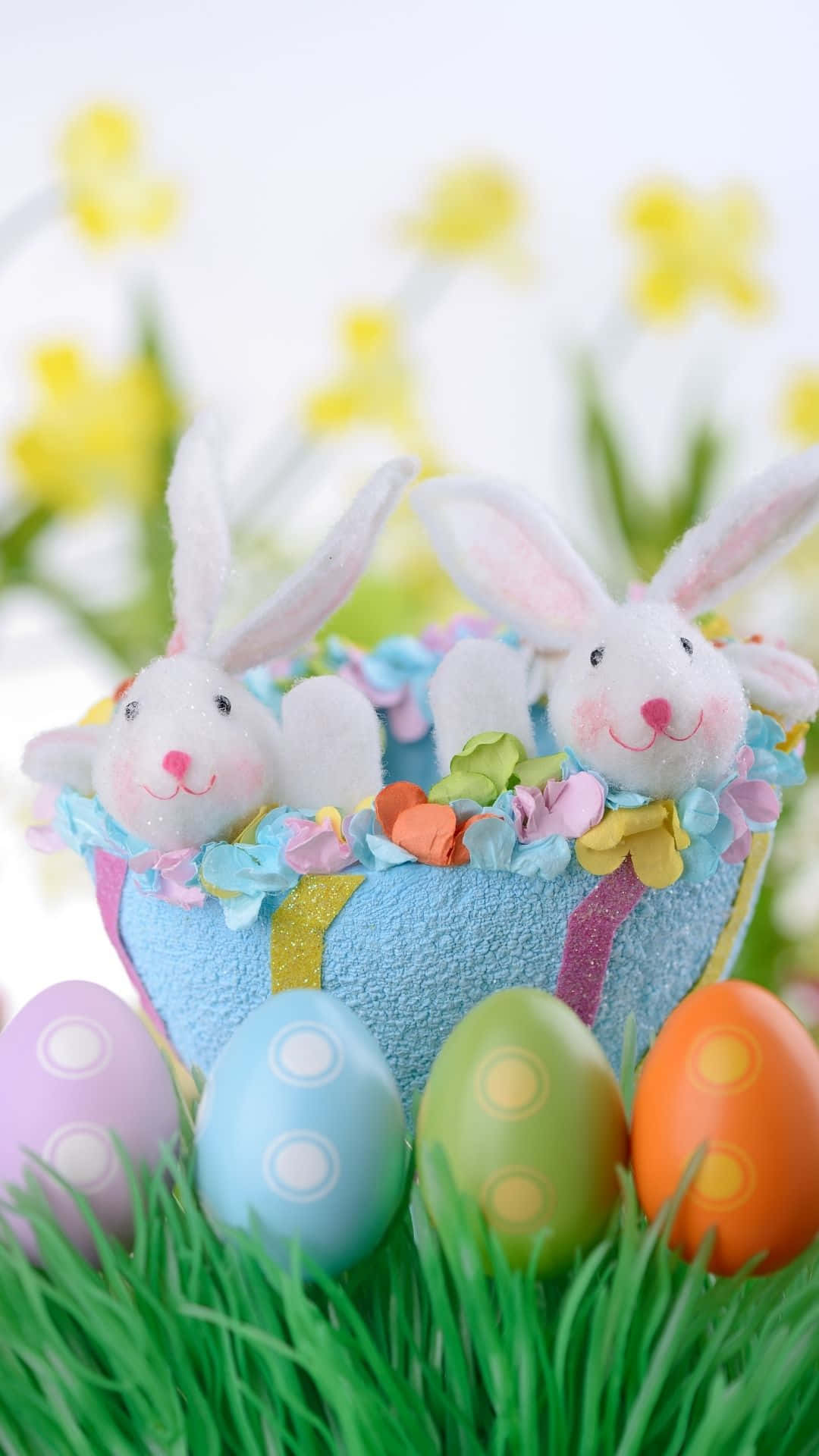 Easter Bunny 桌布 壁紙 — 兩隻毛絨兔子從一個色彩繽紛的復活節籃子中探出頭來，籃子周圍是裝飾蛋，在充滿生機的草地上。