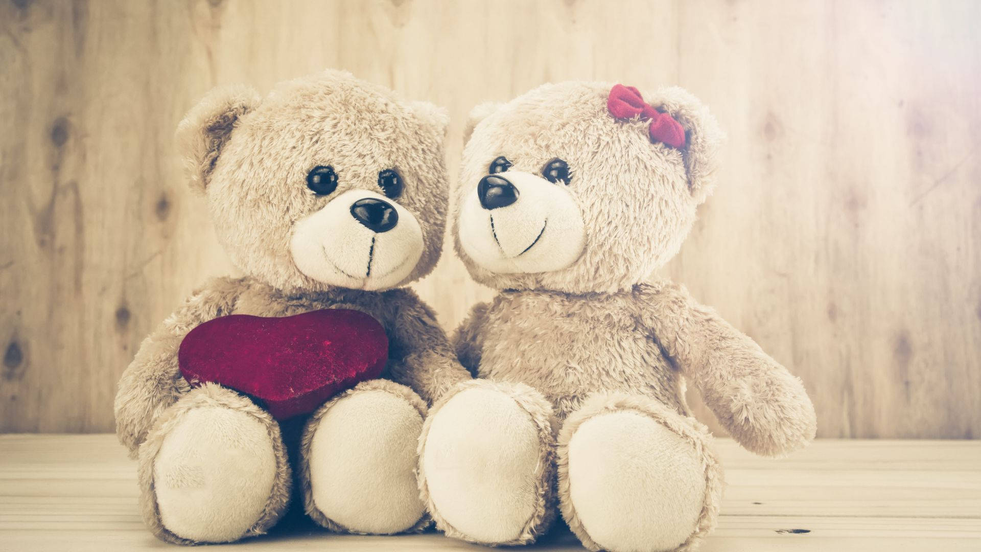 Teddy Bear 桌布 壁紙 — 兩隻毛絨絨的泰迪熊並排坐在木質表面上，一隻拿著紅心，另一隻戴著紅色蝴蝶結。