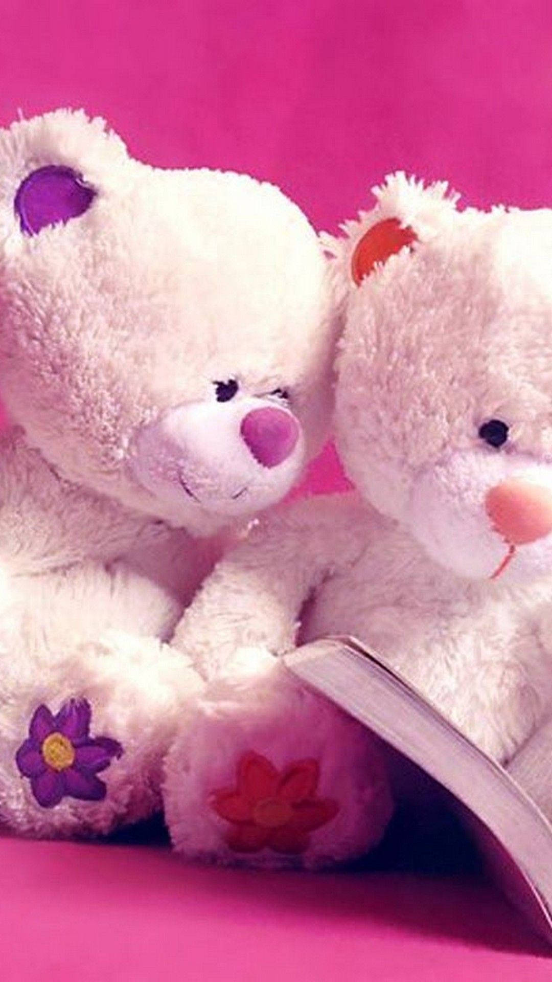 Teddy Bear 桌布 壁紙 — 兩隻毛茸茸的白色泰迪熊，帶有彩色花朵補丁，在鮮豔的粉紅色背景前依偎在一本打開的書上。