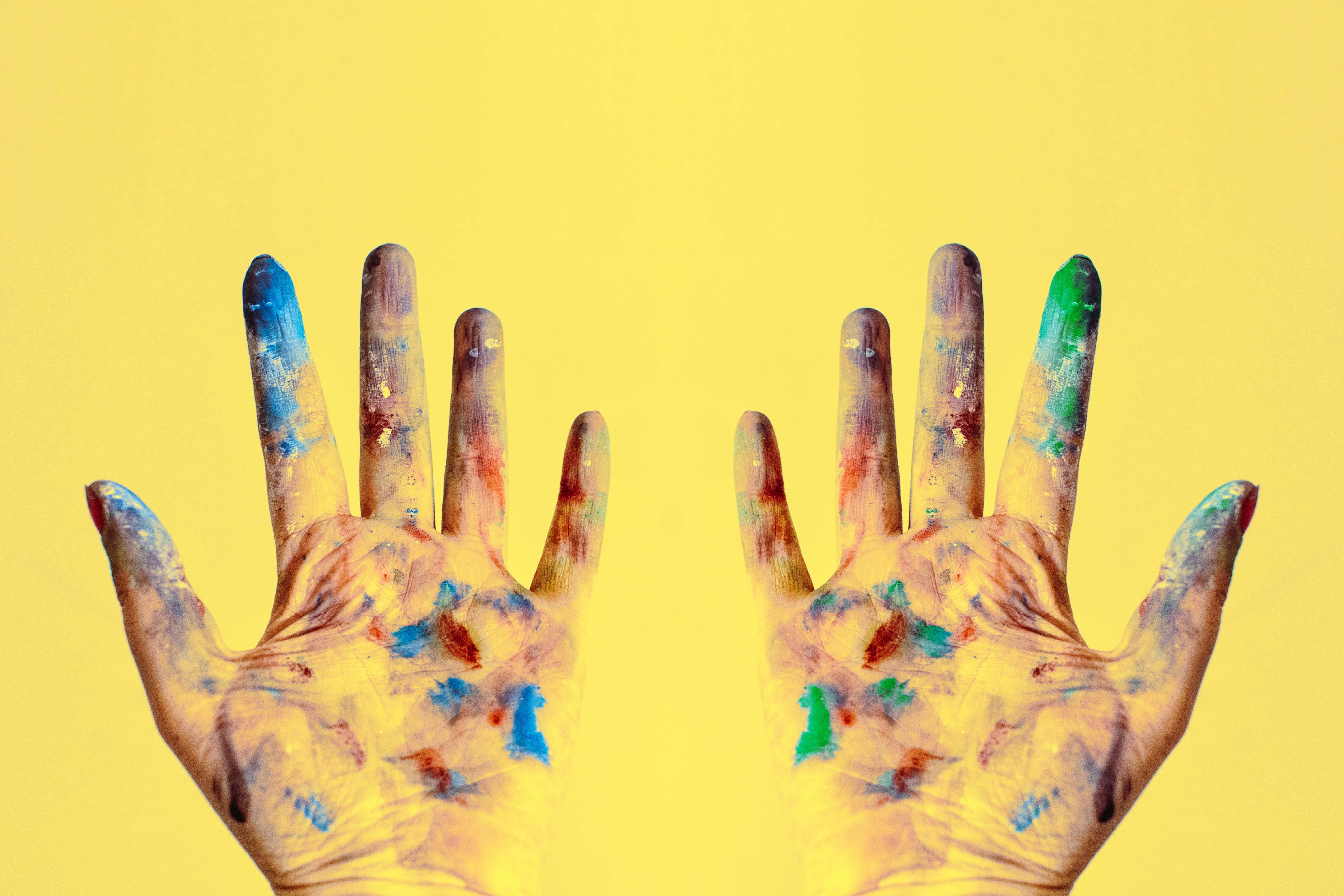 hands 桌布 壁紙 — 兩隻沾滿彩色顏料的手在明亮的黃色背景上張開。