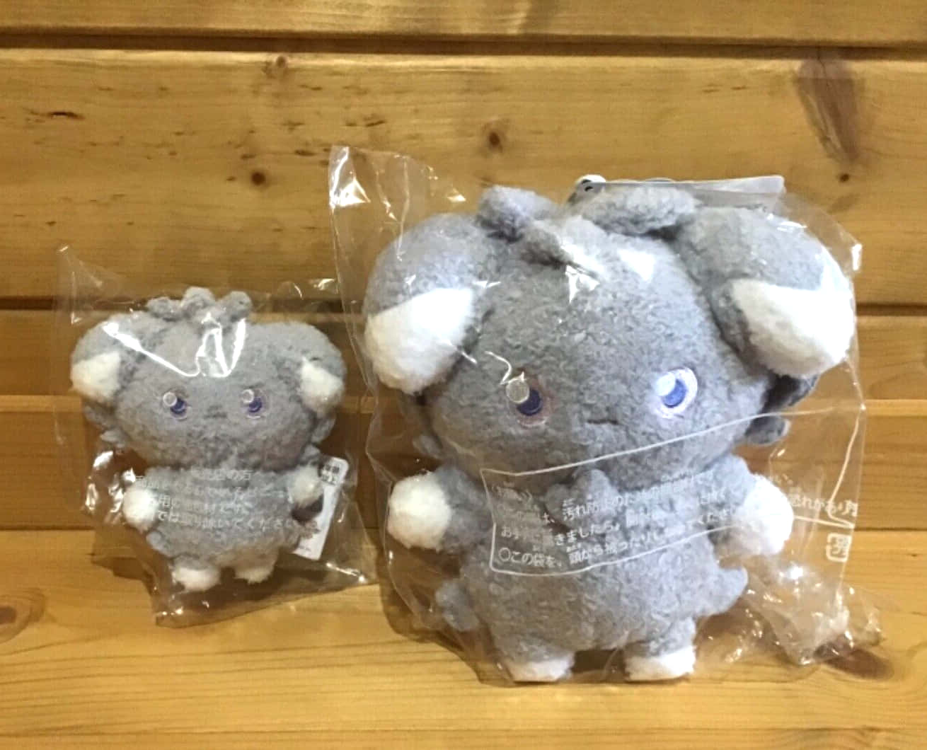 espurr 桌布 壁紙 — 兩隻灰色毛絨玩具大象，白色耳朵和藍色眼睛，坐在木質表面的透明塑膠袋中。