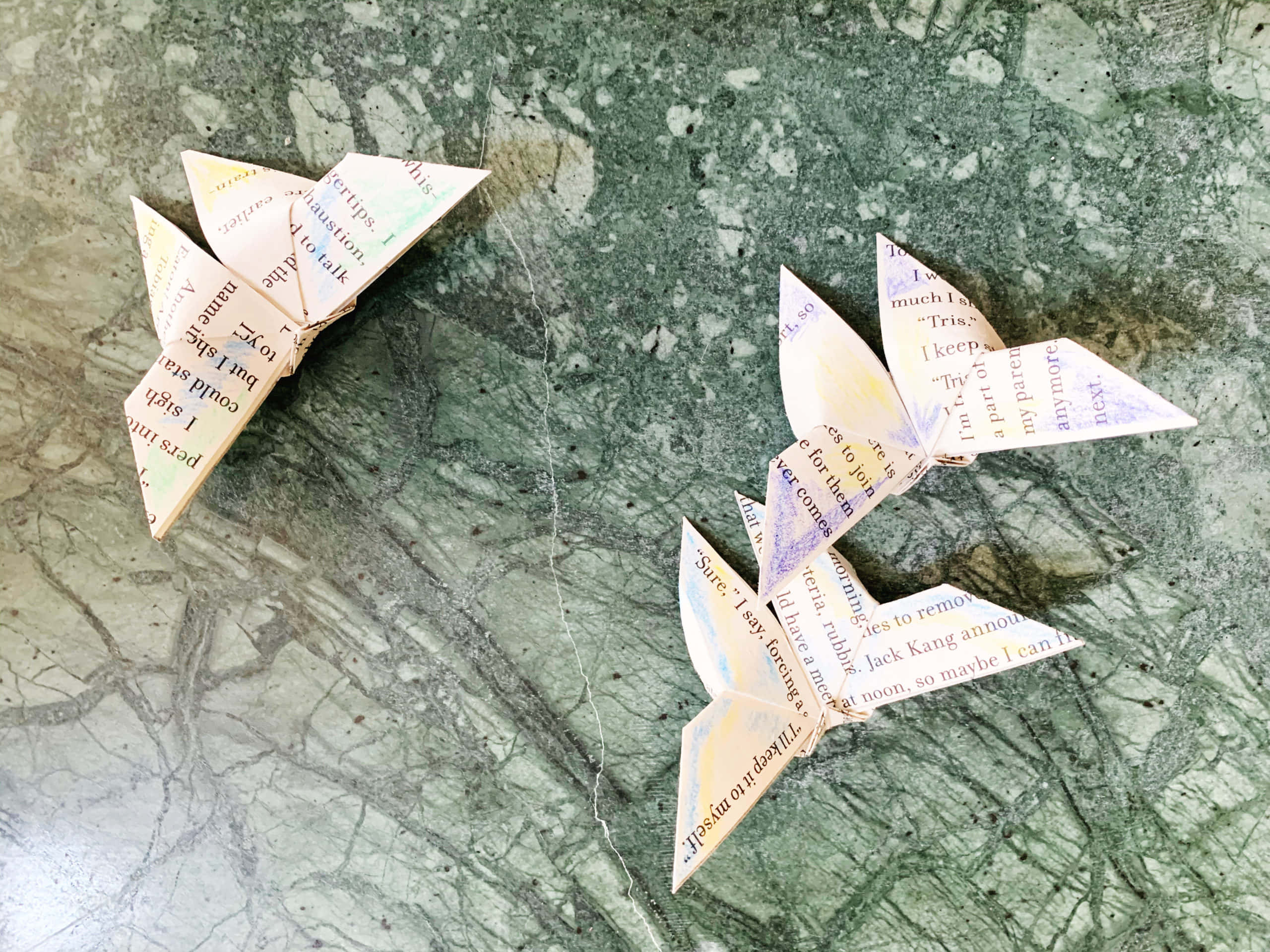 Butterfly Origami 桌布 壁紙 — 兩隻用書頁製成的摺紙蝴蝶停留在帶有印刷文字的綠色大理石紋表面上。