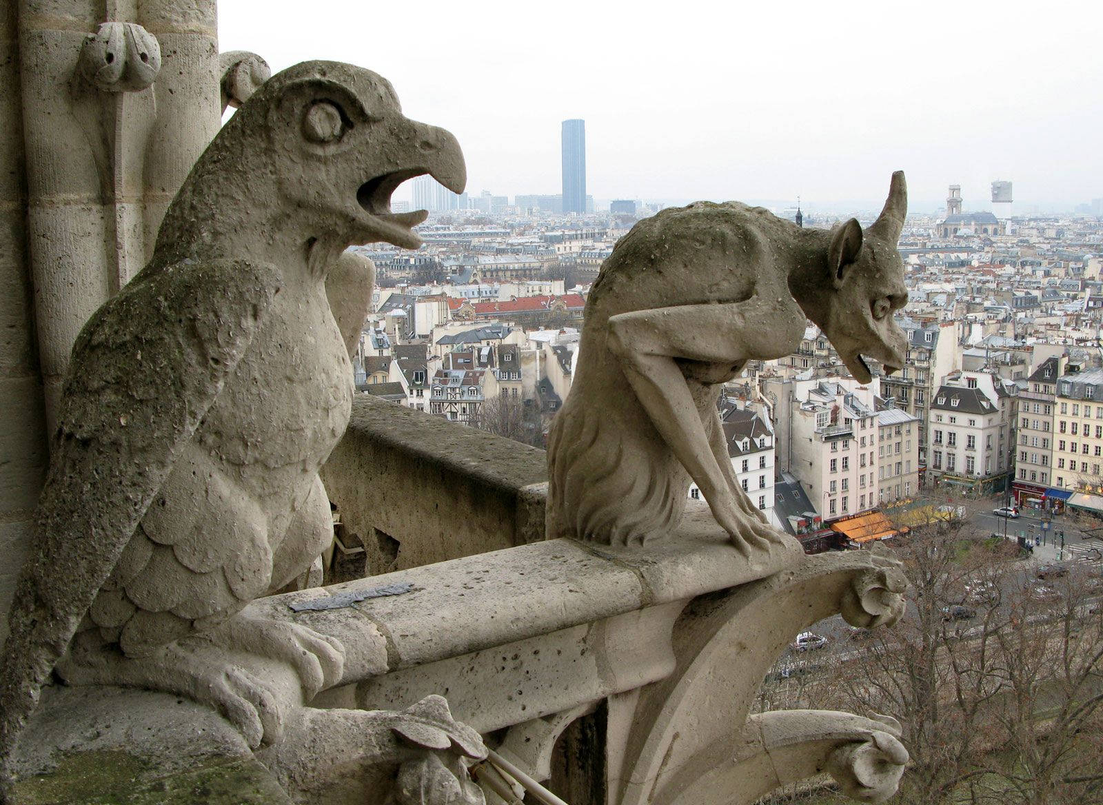 Notre Dame 桌布 壁紙 — 兩隻石像鬼棲息在大教堂的壁架上，俯瞰著陰天籠罩下廣闊的巴黎城市景觀。