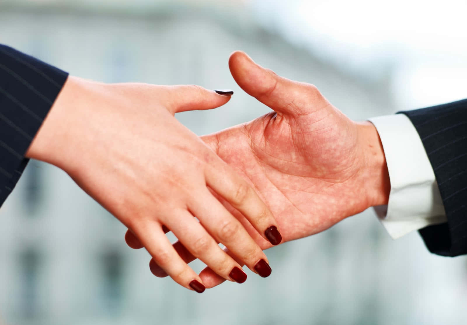 hands 桌布 壁紙 — 兩隻穿著西裝的商業手在模糊的城市背景下緊緊握手。