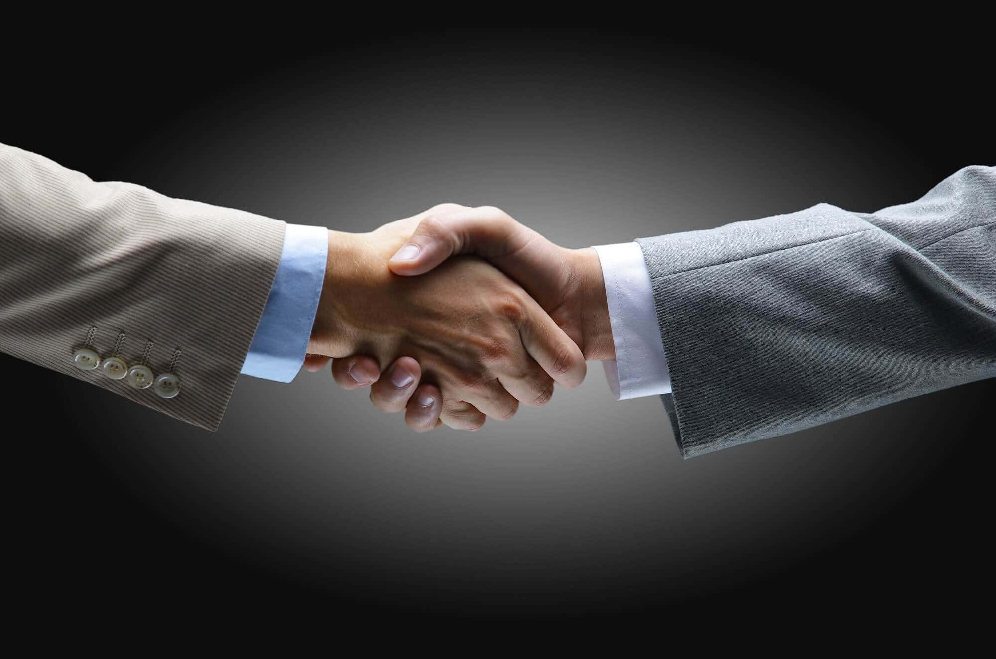 hands 桌布 壁紙 — 兩隻穿著西裝的商業手在深色漸變背景前堅定地握手。