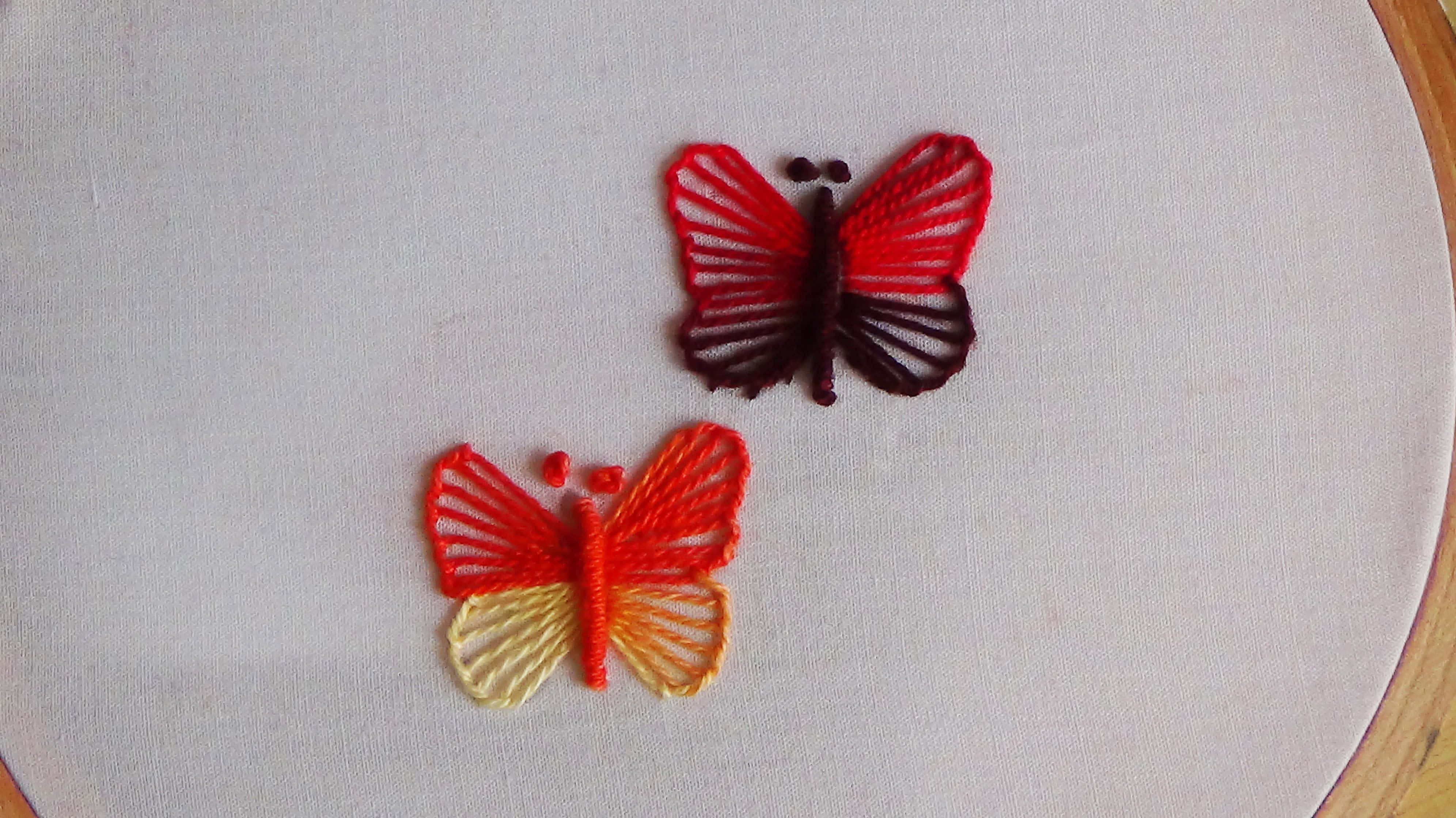 Butterfly Stitch 桌布 壁紙 — 兩隻精緻刺繡的蝴蝶，以紅色和橙色色調，安放在木製刺繡框內的白色布料上。