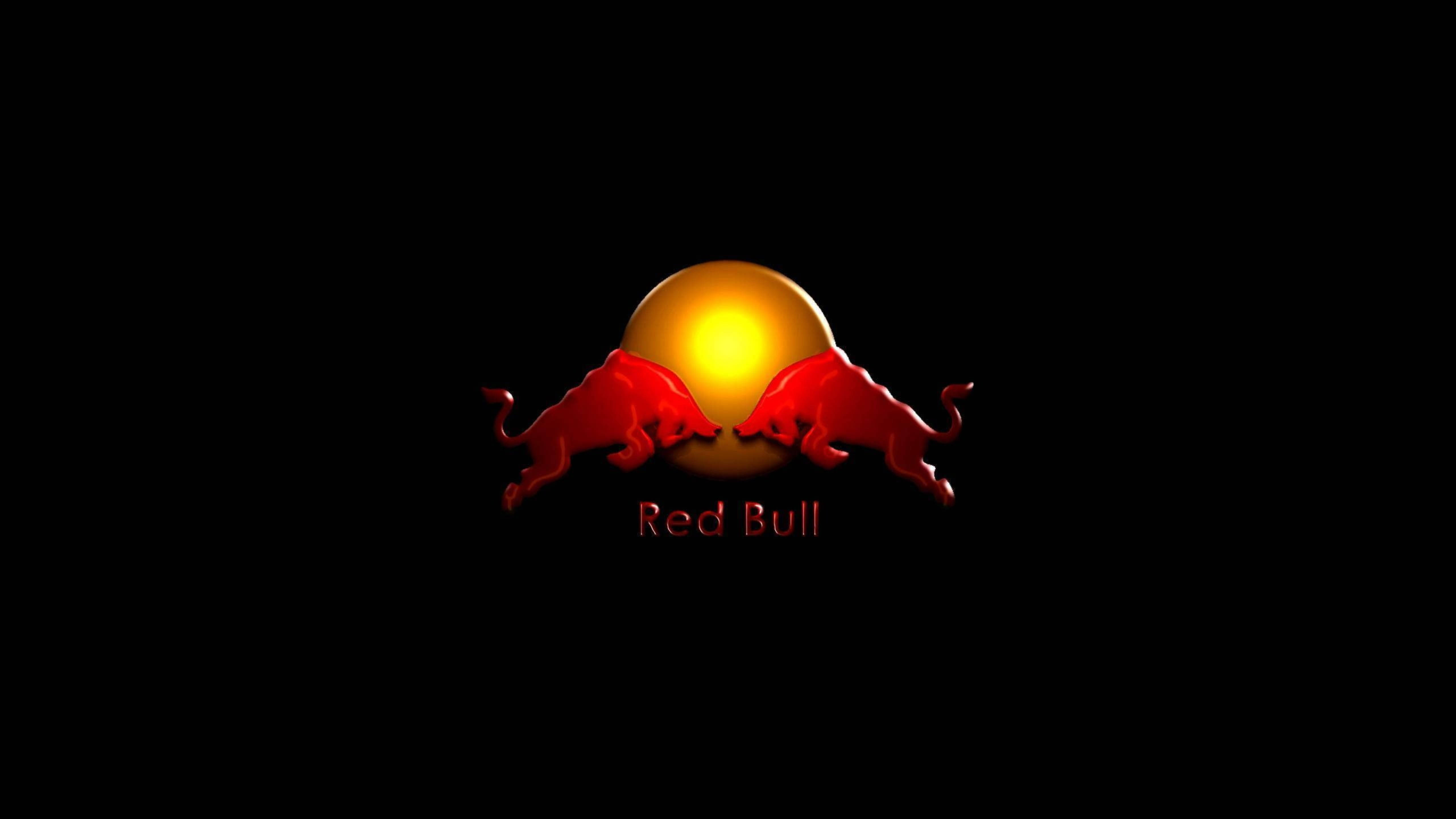 bull 桌布 壁紙 — 兩隻紅色衝鋒的公牛在發光的金色太陽周圍面對面，黑色背景，下方有「Red Bull」文字。