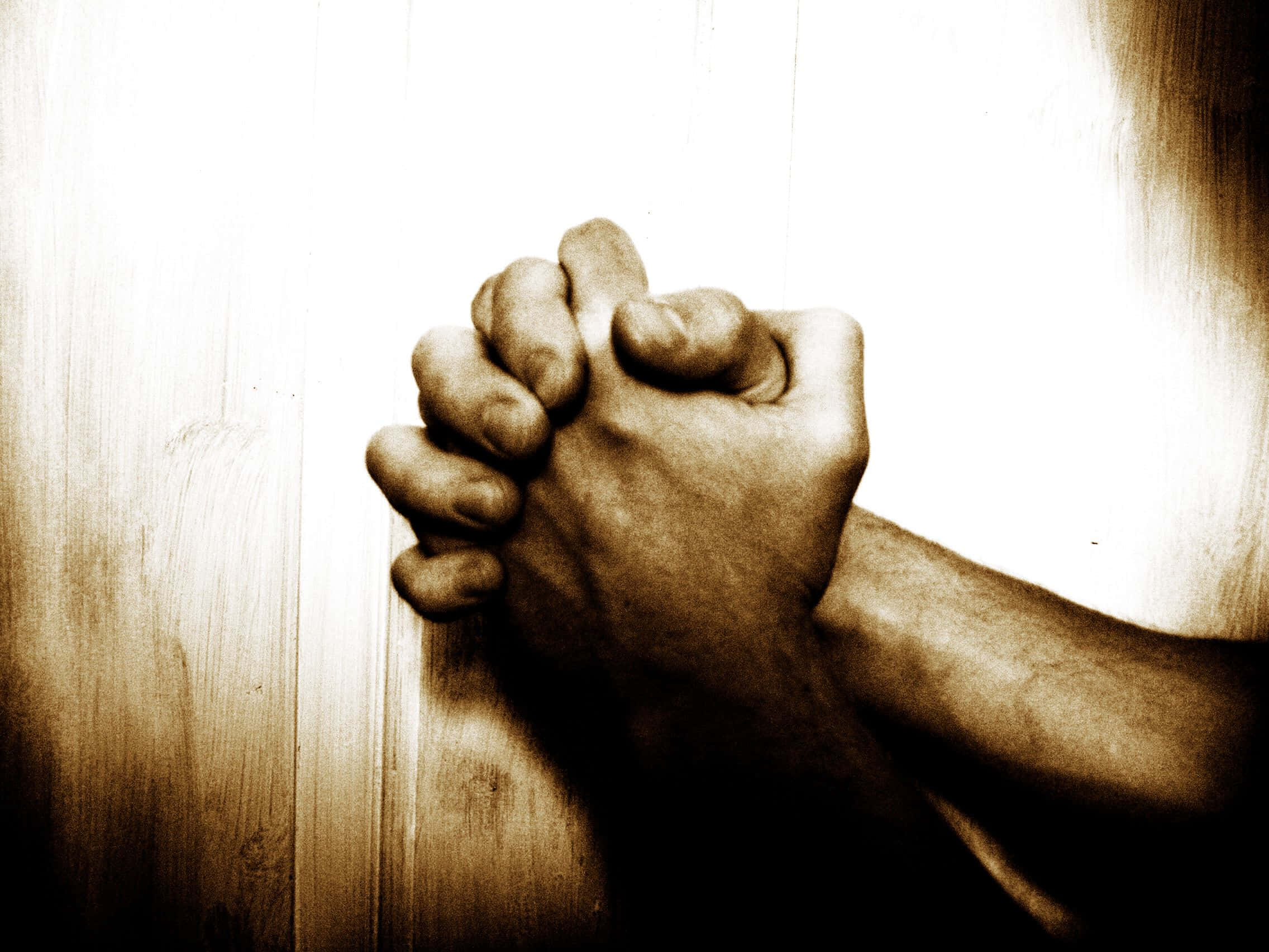 Praying 桌布 壁紙 — 兩隻緊握的手在木質表面上祈禱，呈現溫暖的棕褐色調。