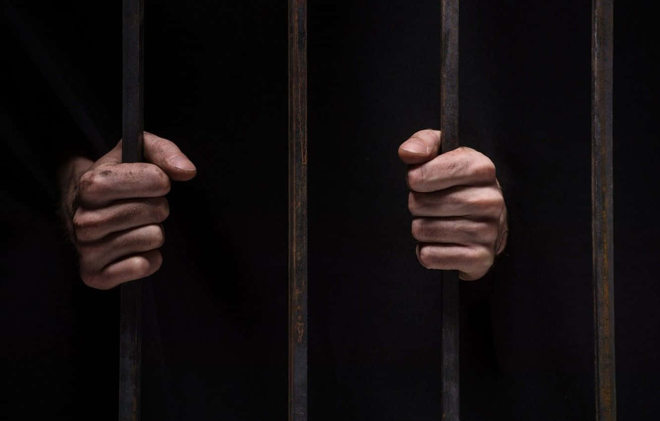 Prison Cell 桌布 壁紙 — 兩隻緊握的拳頭抓住生鏽的金屬欄杆，背景漆黑一片，傳達出禁錮與絕望。