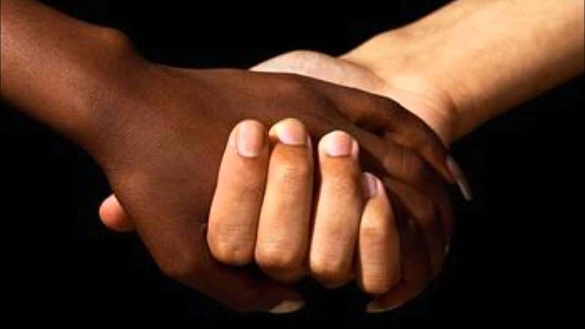 Interracial 桌布 壁紙 — 兩隻膚色對比的手在黑色背景前緊握，象徵團結。