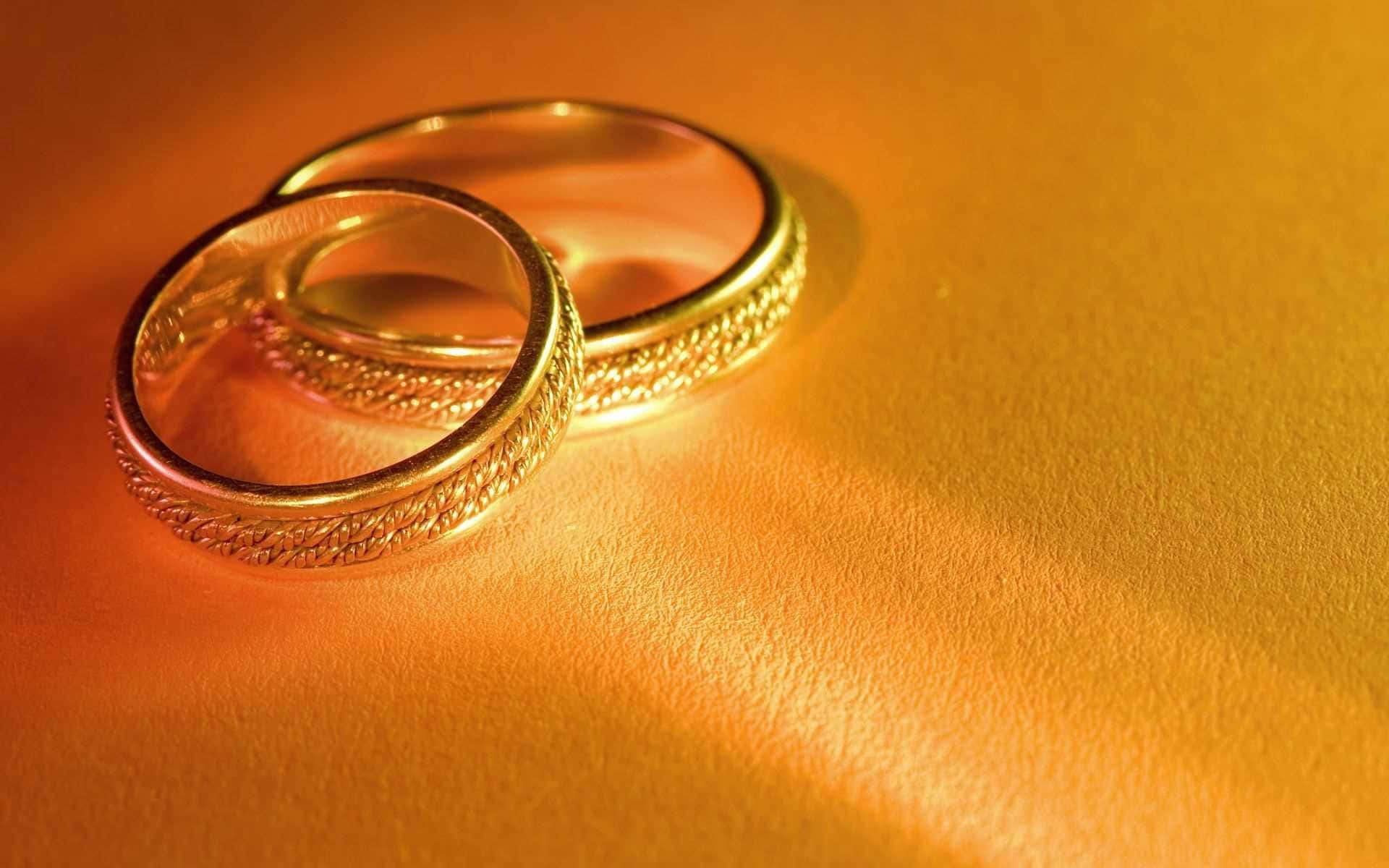 Jewelry Design 桌布 壁紙 — 兩隻華麗的金色結婚戒指放在溫暖的紋理表面上，沐浴在金色的光線中。