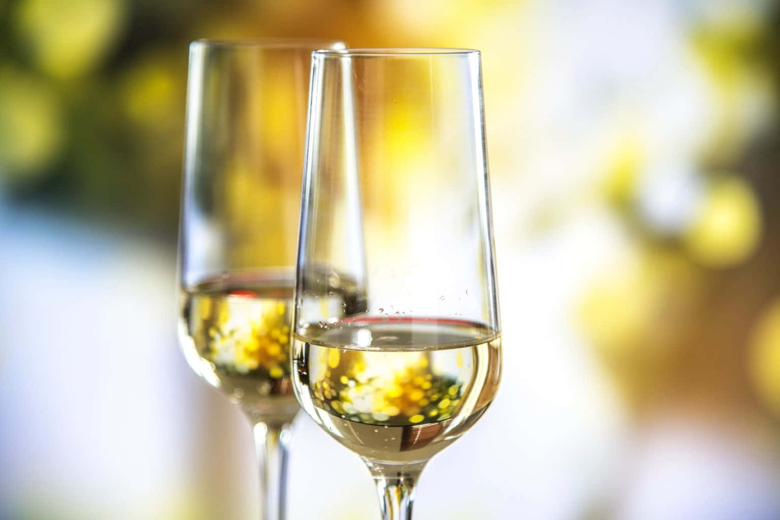 葡萄酒 桌布 壁紙 — 兩隻裝滿冒泡金色液體的香檳杯，在溫暖模糊的黃色散景燈光背景下，以柔和焦點呈現。