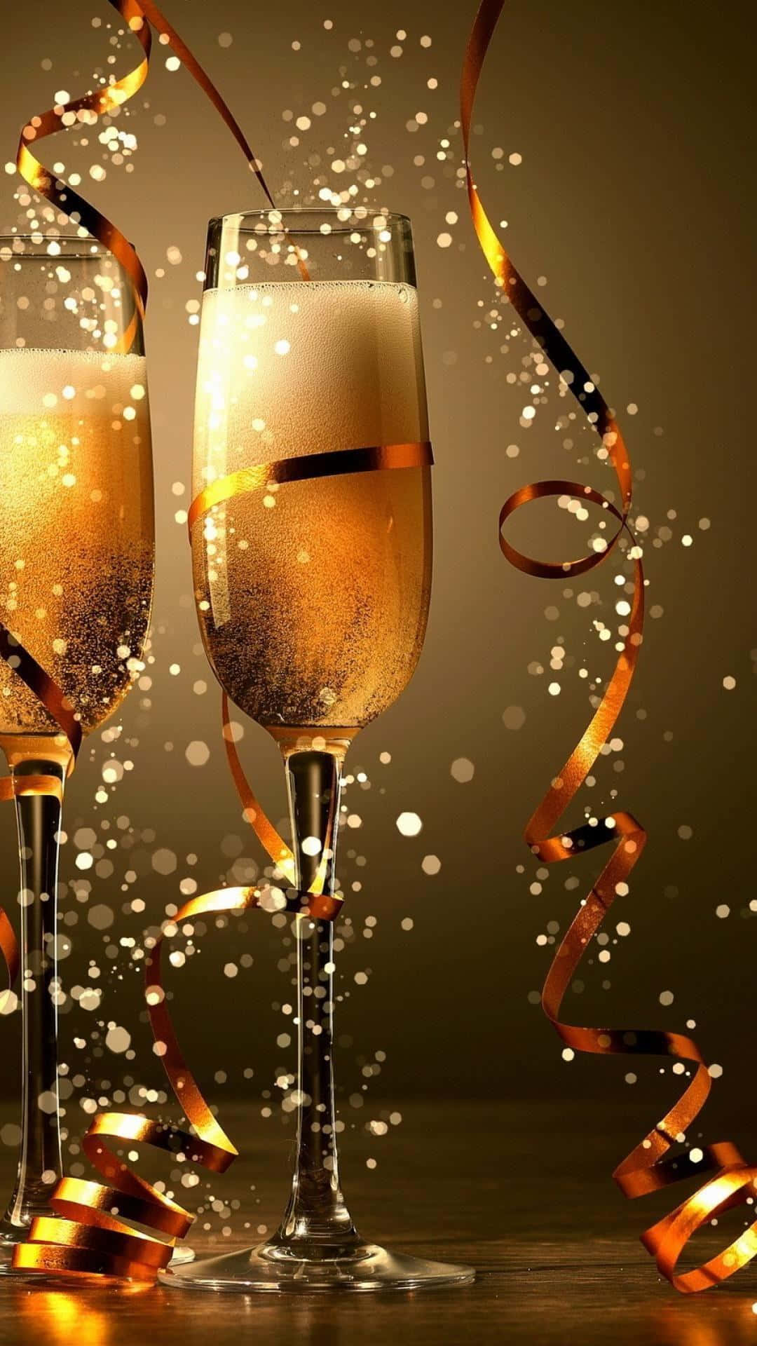New Year 桌布 壁紙 — 兩隻裝滿冒泡金色液體的香檳杯，在溫暖的棕色背景下閃爍著閃閃發光的五彩紙屑和旋轉的金色絲帶。