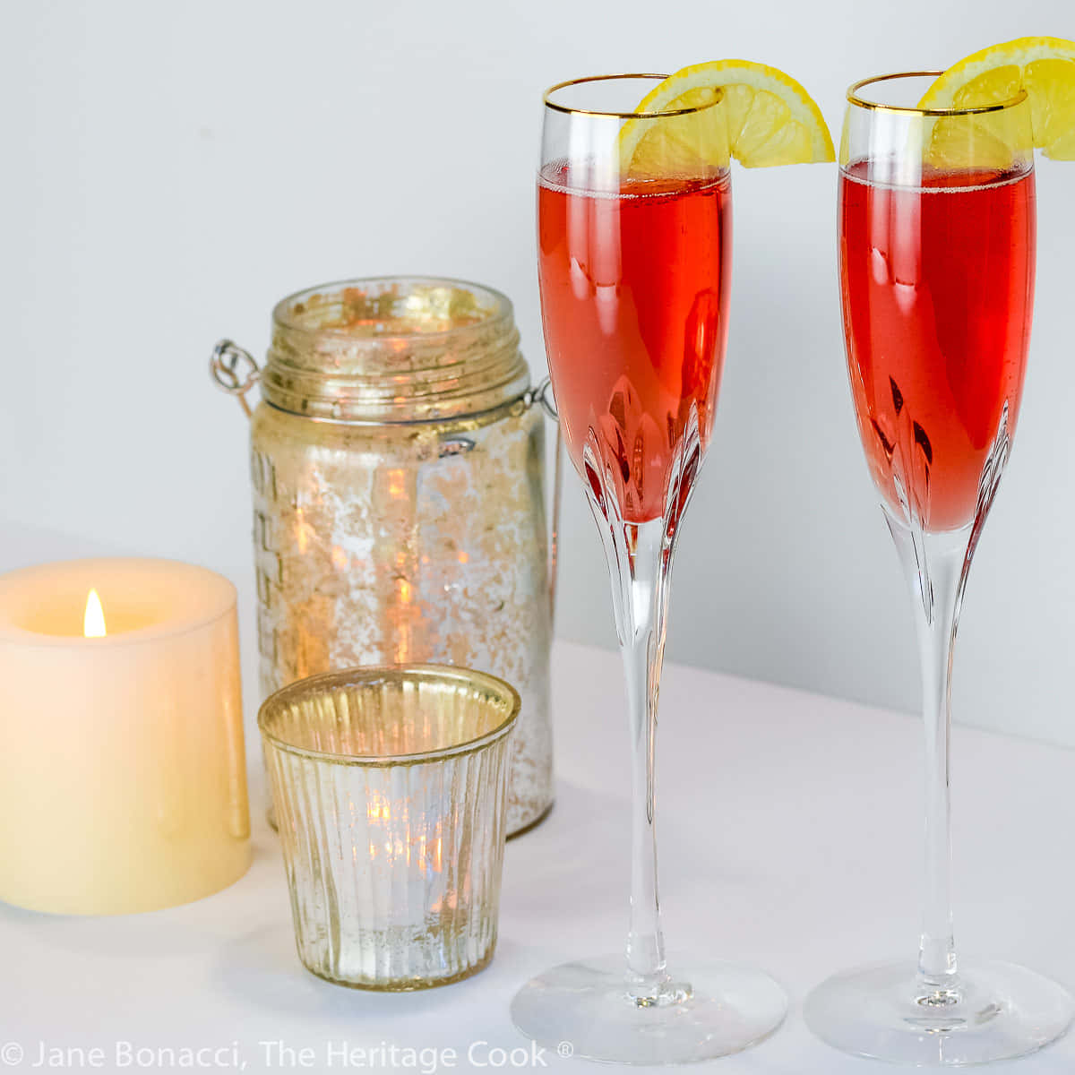Beautiful Drink 桌布 壁紙 — 兩隻香檳杯盛滿鮮紅色雞尾酒，飾以檸檬片，旁邊有發光的蠟燭和水銀玻璃罐。