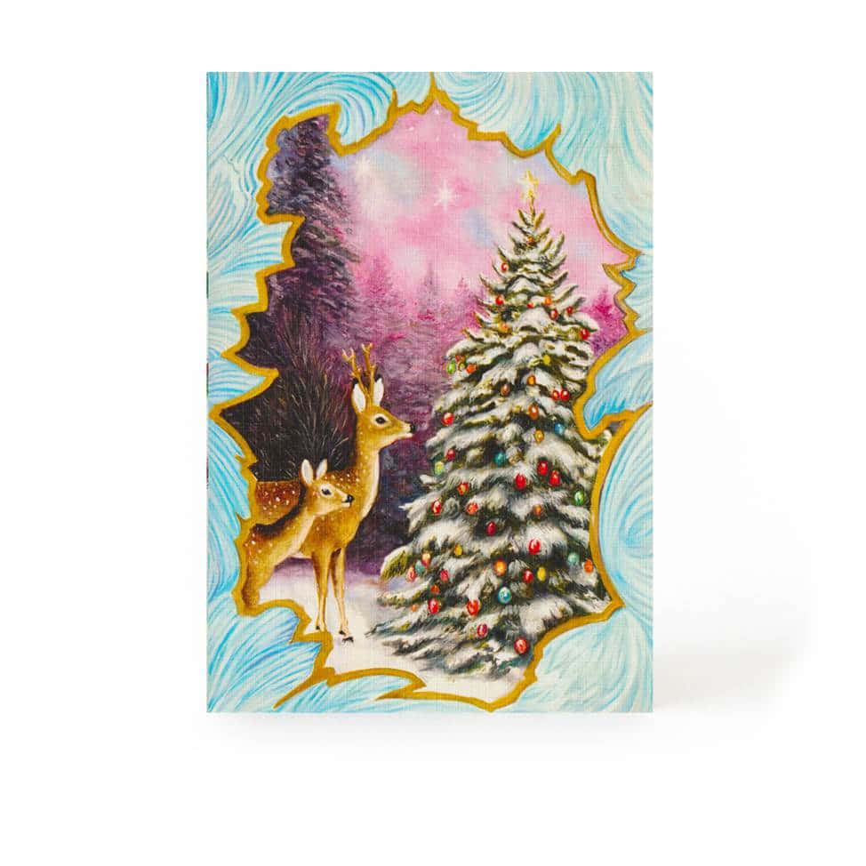 Christmas Card 桌布 壁紙 — 兩隻鹿凝視著一棵被雪覆蓋的聖誕樹，樹上裝飾著色彩繽紛的飾物，背景是粉紅色的星空。