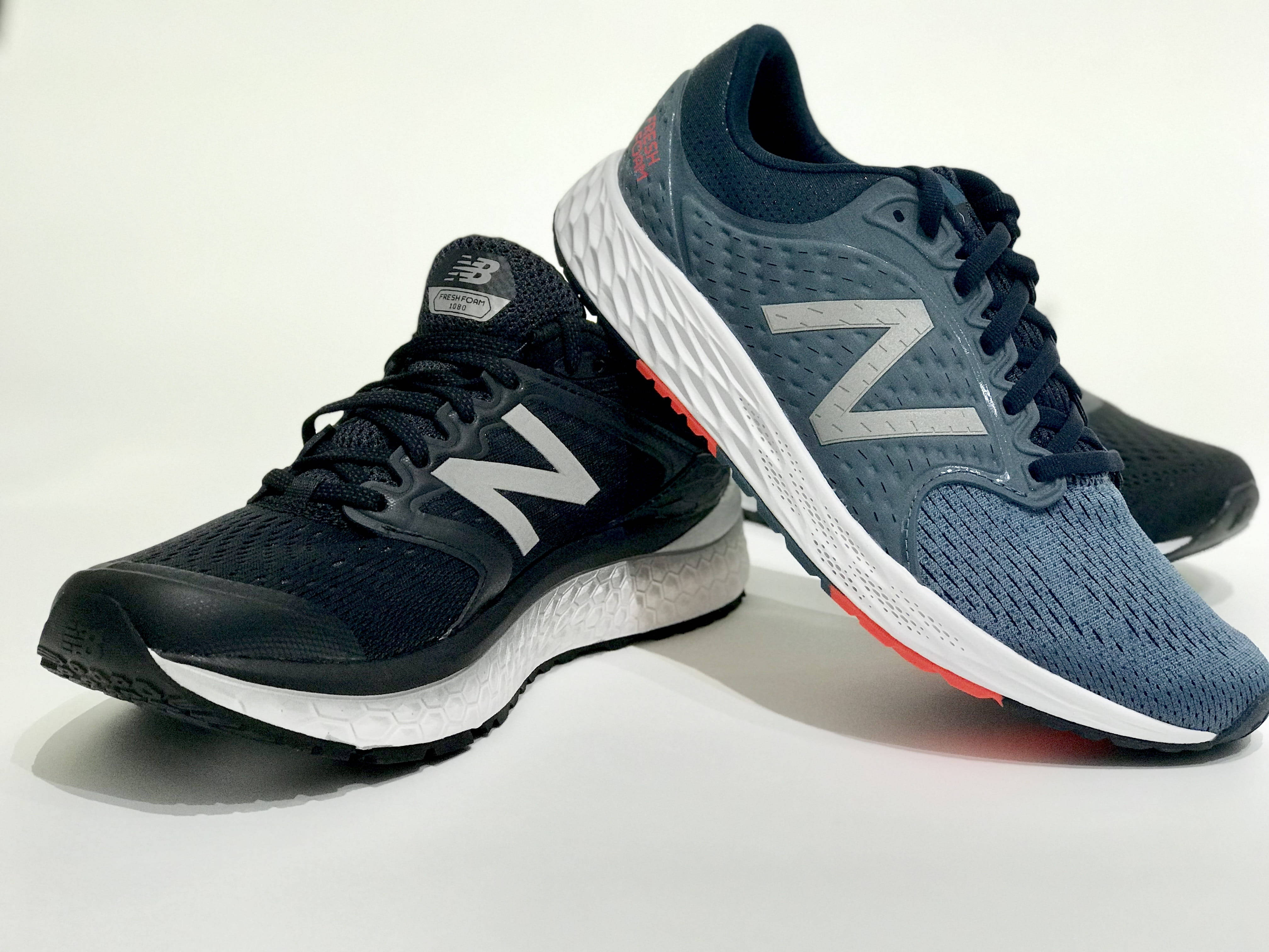 New 桌布 壁紙 — 兩雙New Balance跑鞋，黑色和深藍色，白色鞋底和紅色點綴，傾斜放置在乾淨的白色表面上。