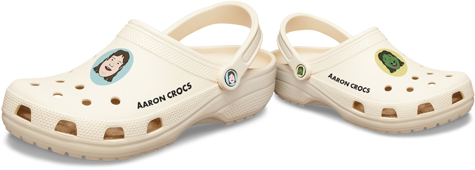 Crocs 桌布 壁紙 — 兩雙奶油色Crocs木屐，帶有卡通角色貼片和「Aaron Crocs」文字，背景為黑色。