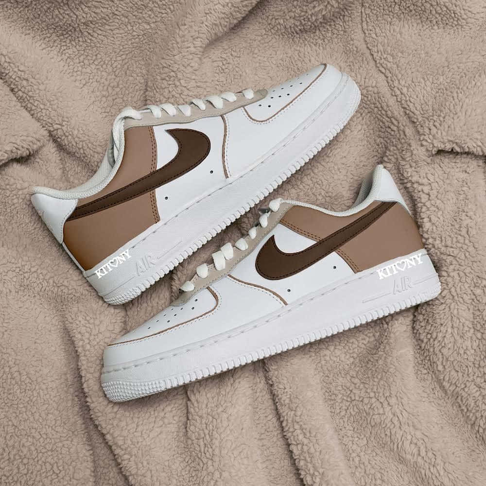 Nike Air Force 桌布 壁紙 — 兩雙帶有 'KITONY' 品牌標誌的白色和棕色 Nike Air Force 1 運動鞋，放在柔軟的米色抓絨毯上。