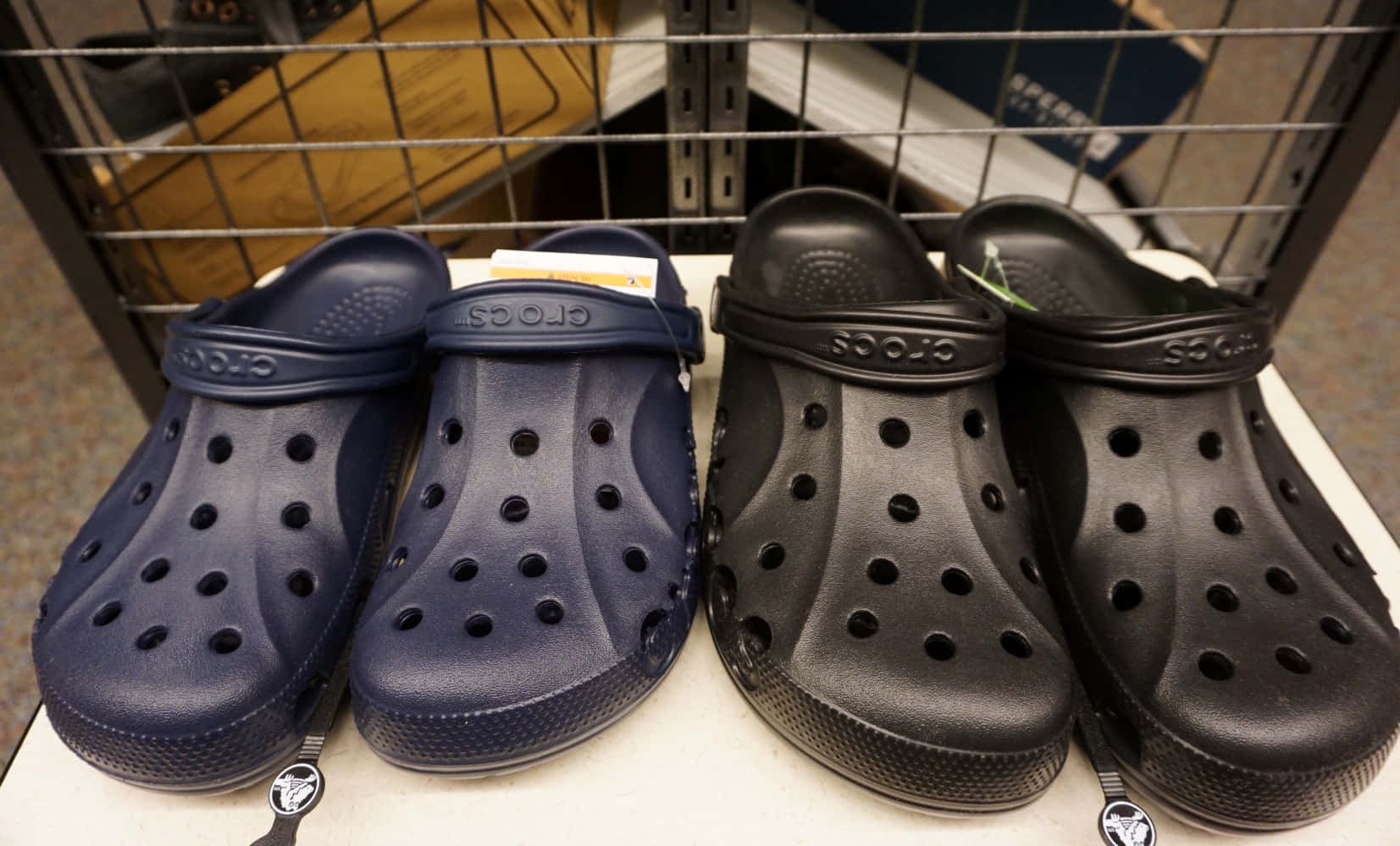 Crocs 桌布 壁紙 — 兩雙海軍藍和黑色的Crocs克洛格鞋並排展示在零售店的白色層架上。