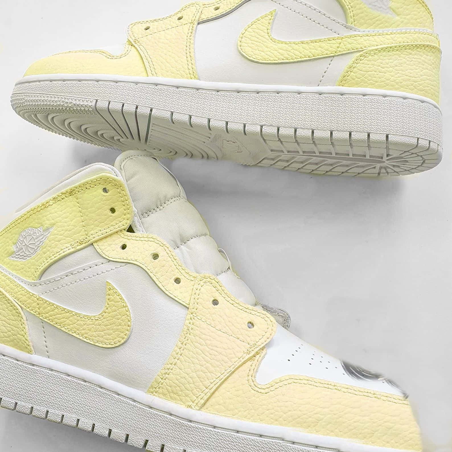 Yellow Jordan 桌布 壁紙 — 兩雙淡黃色和白色的高筒運動鞋，帶有紋理皮革和可見縫線，傾斜放置在純白色背景上。