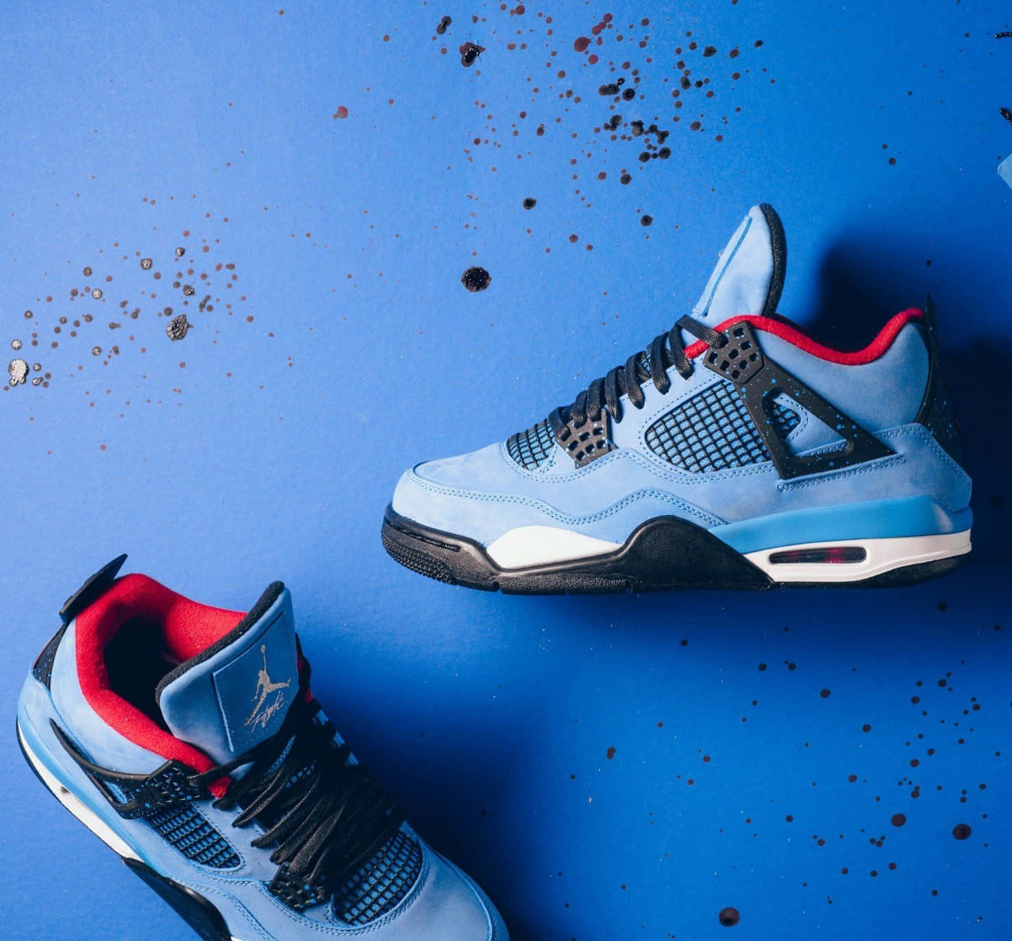 淺藍色Jordan 4運動鞋，帶有紅色點綴，藍色背景上有油漆飛濺。 — Air Jordan 1 壁紙