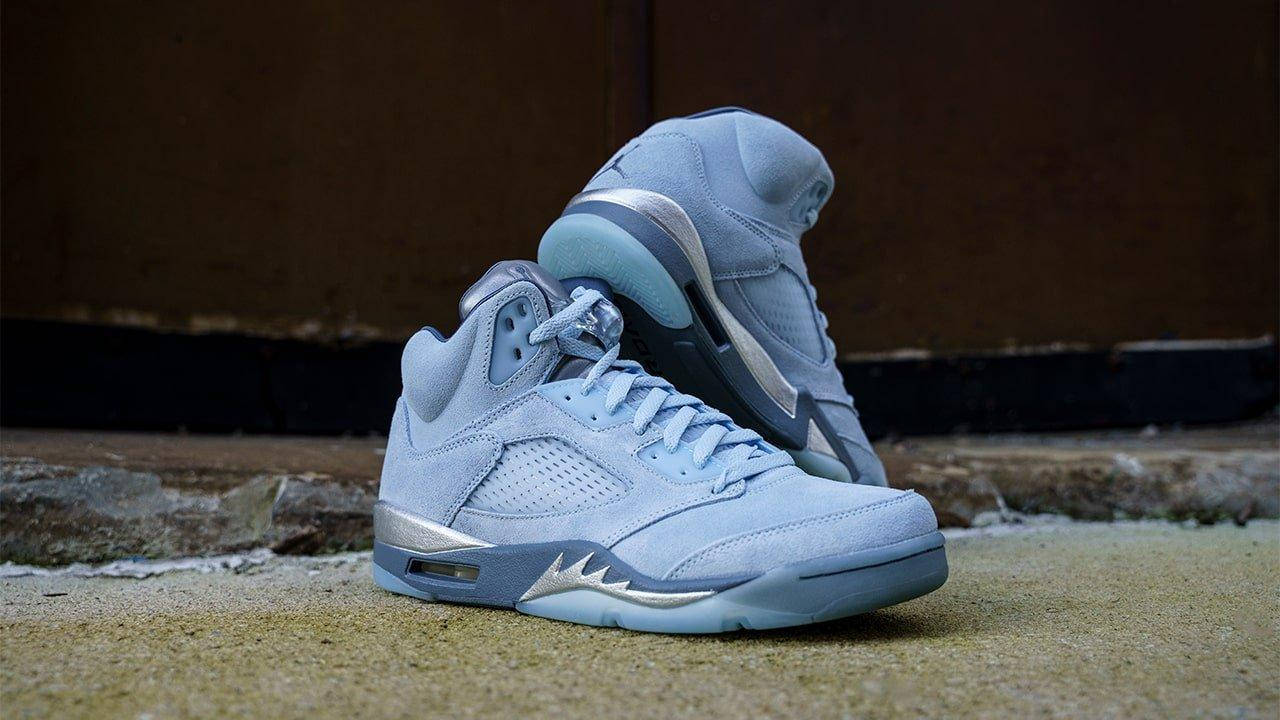 高清 桌布 壁紙 — 兩雙淺藍色麂皮 Air Jordan 5 運動鞋，帶有銀色點綴，放在混凝土階梯上，背景是深色木牆。