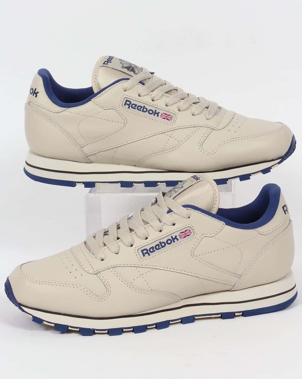 銳步 桌布 壁紙 — 兩雙米色 Reebok Classic 運動鞋，帶有藍色點綴，展示在白色方塊上，背景為純白色。