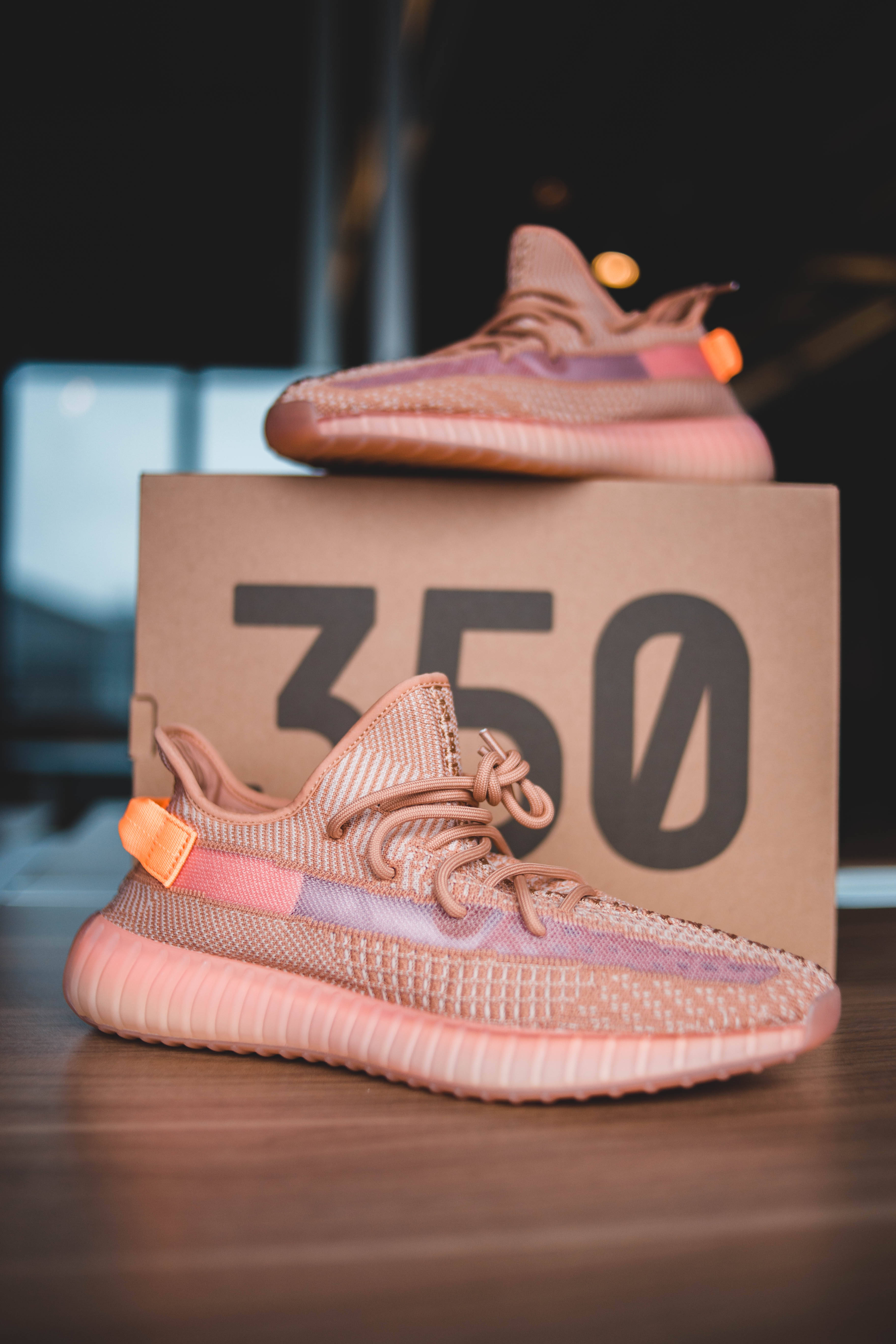 Sneaker 桌布 壁紙 — 兩雙粉紅色和橙色的Yeezy Boost 350運動鞋放在它們的品牌盒子上，置於木質表面，背景燈光模糊。