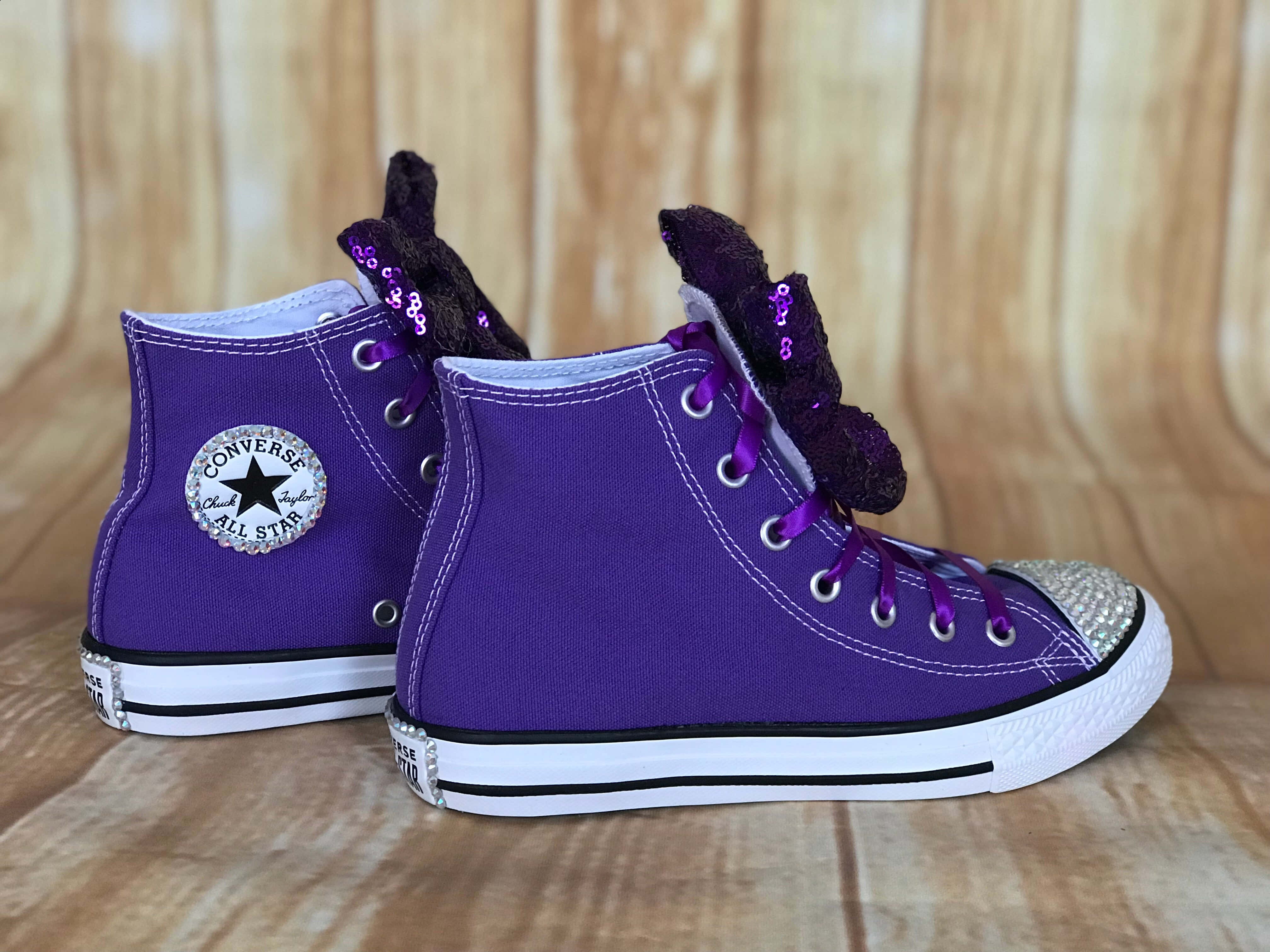 Purple Shoes 桌布 壁紙 — 兩雙紫色Converse高筒運動鞋，帶有亮粉蝴蝶結和水鑽鞋頭，放在木地板上。