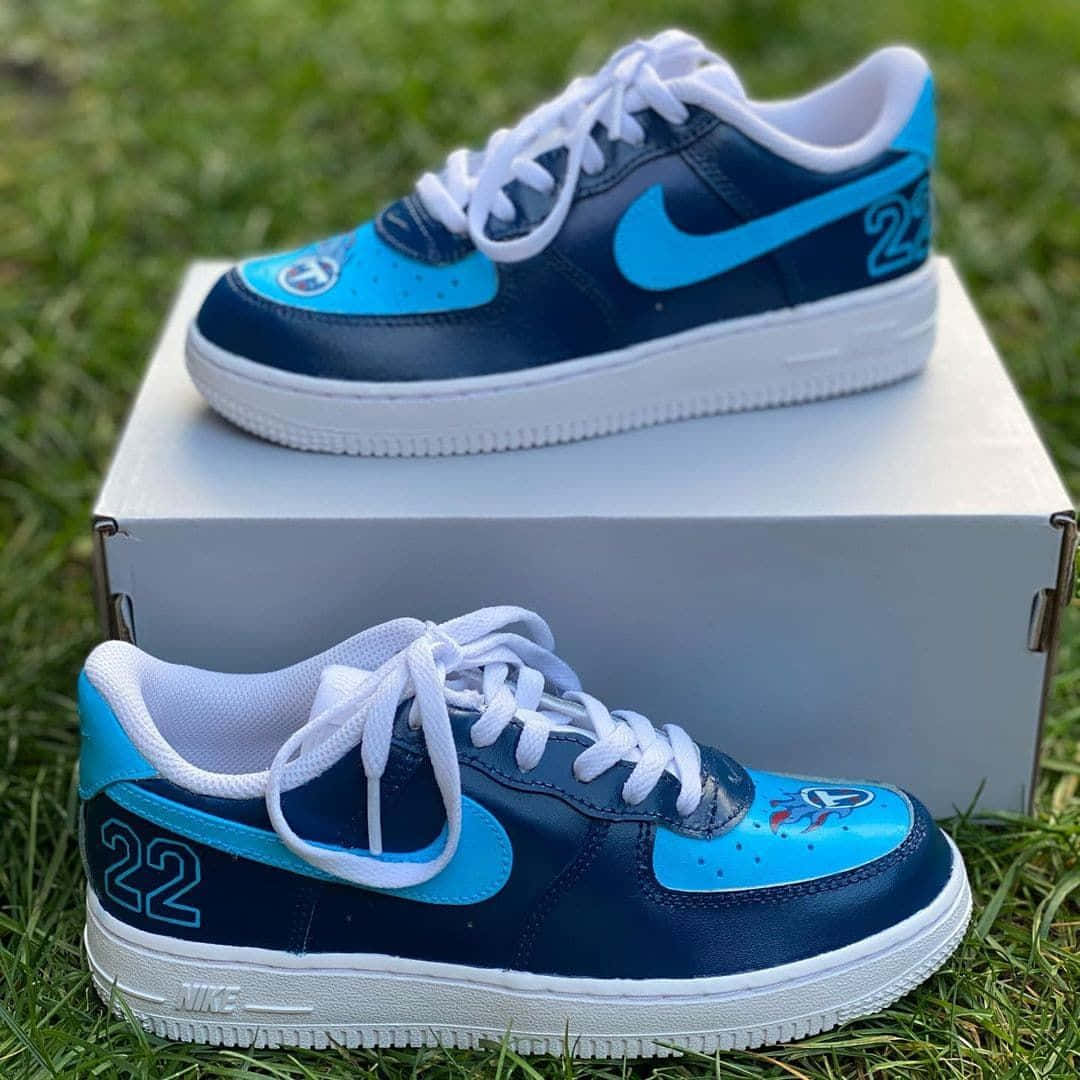 Nike Air Force 桌布 壁紙 — 兩雙訂製的藍白Nike Air Force 1運動鞋，帶有22號和球隊標誌，放置在綠色草地上的鞋盒上。