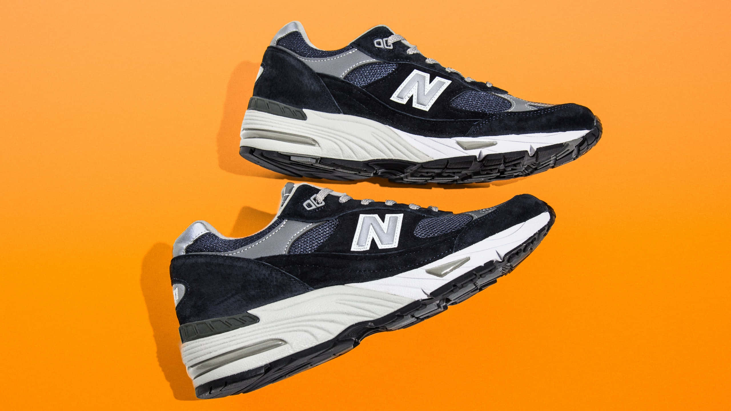 New Balance 桌布 壁紙 — 兩雙黑色New Balance運動鞋搭配白色鞋底，在鮮豔的橙色背景上漂浮。