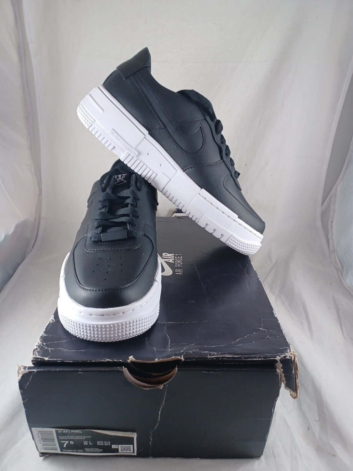 Nike Air Force 桌布 壁紙 — 兩雙黑色Nike Air Force 1運動鞋，白色鞋底，放在一個磨損的黑色鞋盒上，背景為白色。