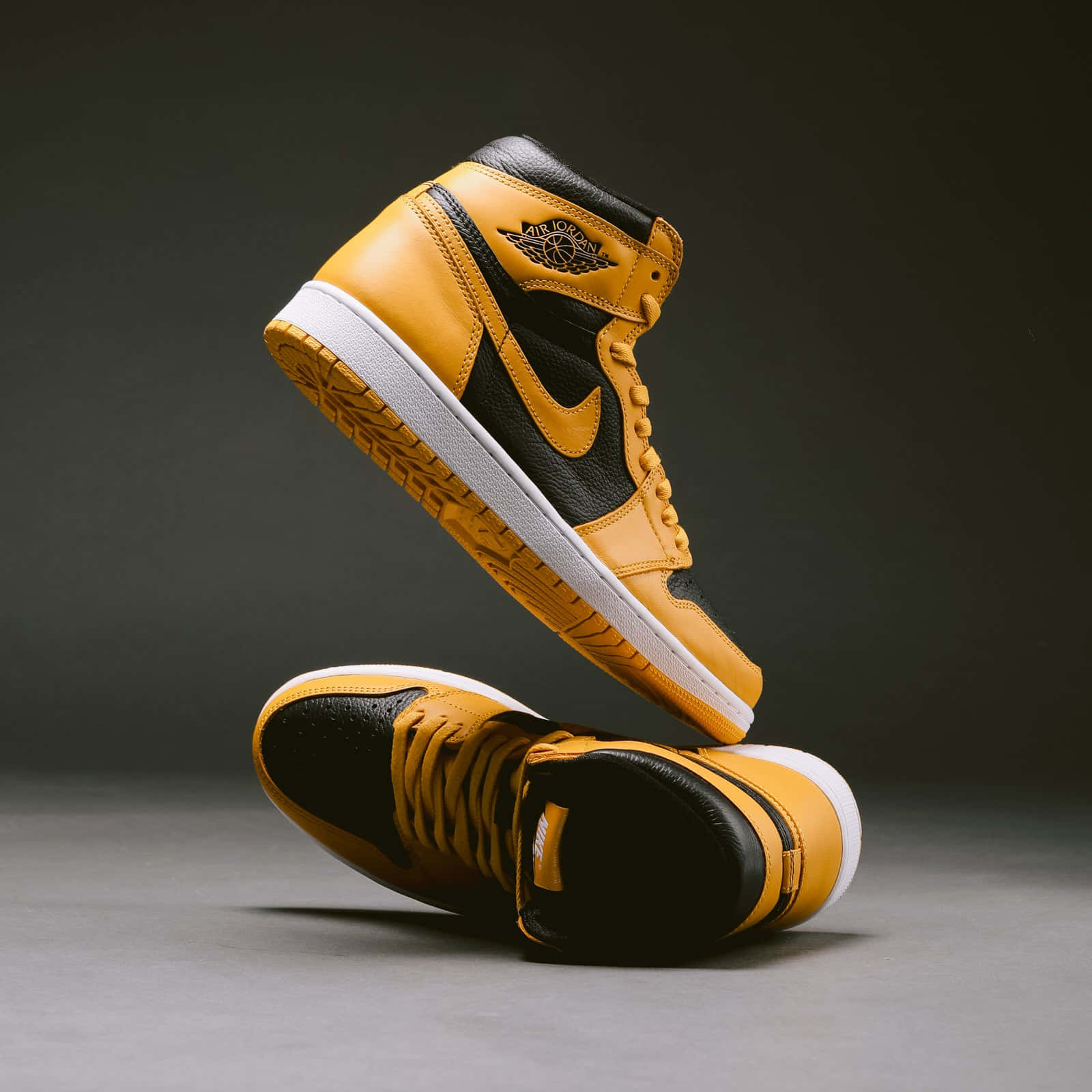 Yellow Jordan 桌布 壁紙 — 兩雙黑色和金色的Air Jordan 1運動鞋懸浮在空中，背景是深色攝影棚。
