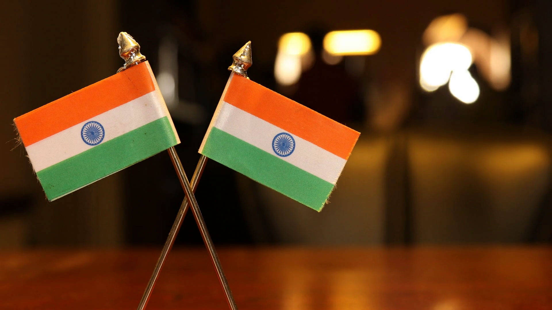Indian 桌布 壁紙 — 兩面交叉的微型印度國旗放在木桌上，背景有溫暖的散景燈光。