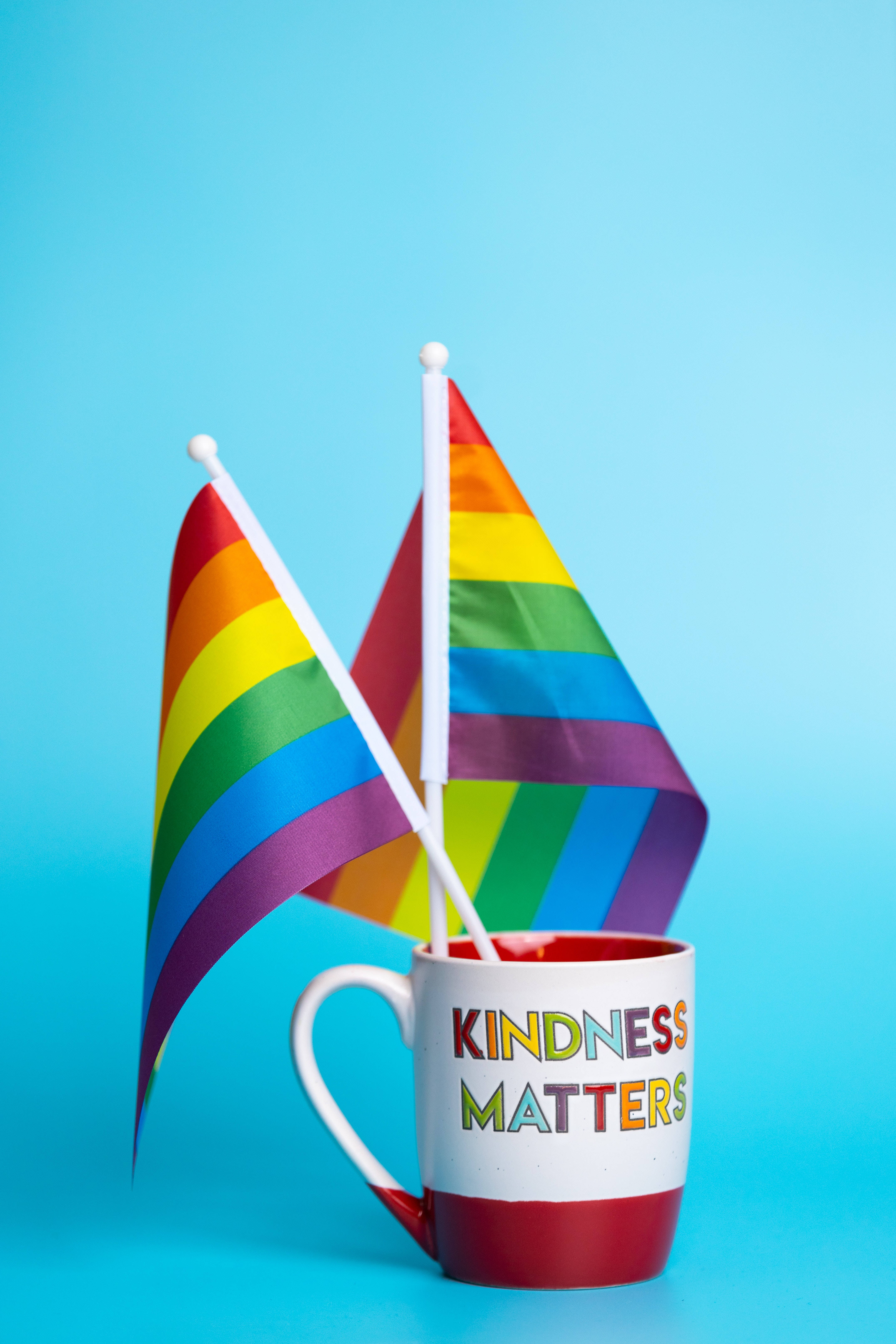 彩虹旗 桌布 壁紙 — 兩面彩虹旗從一個寫有 kindness matters 的杯子上飄揚，背景為純藍色。