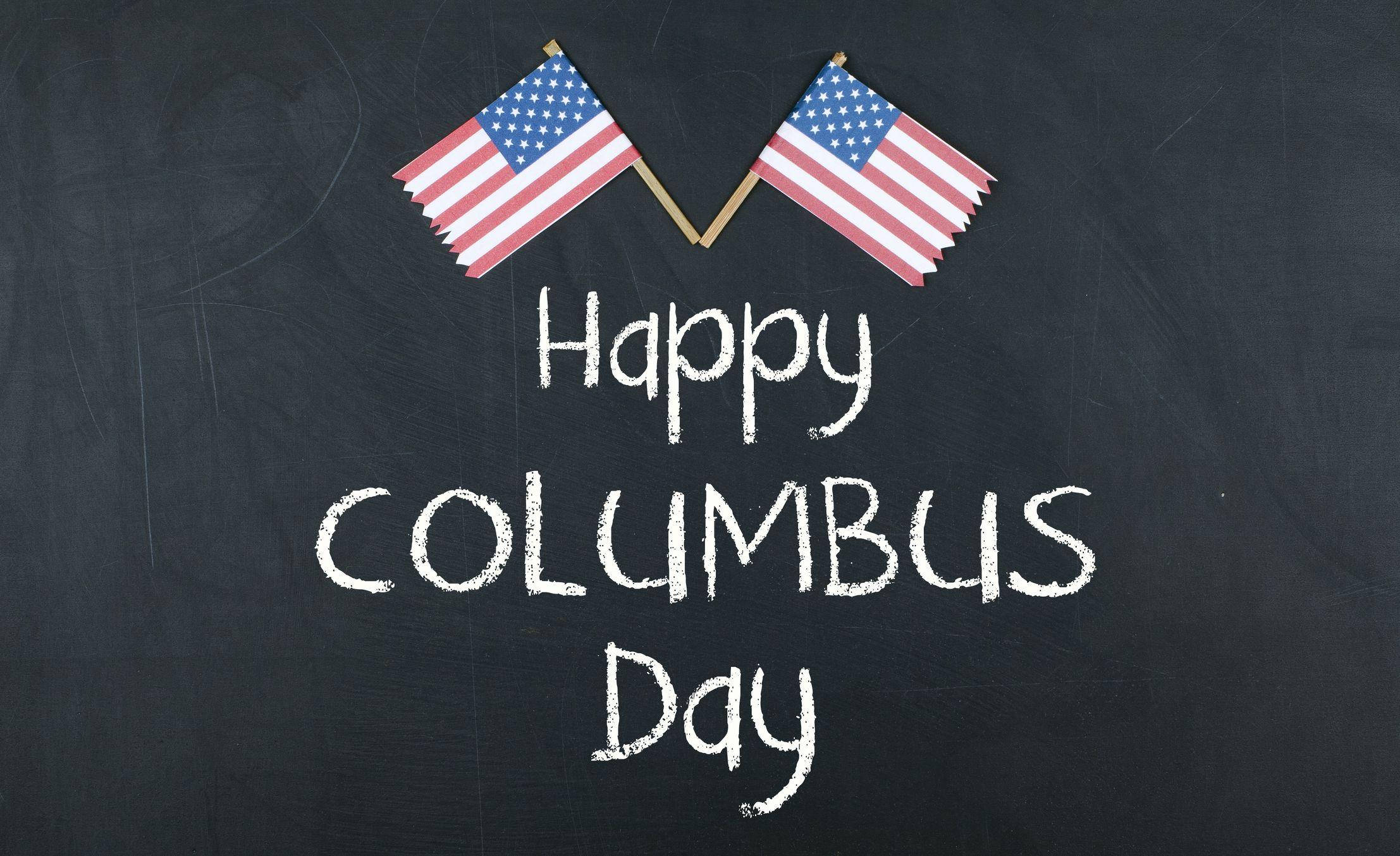 Columbus Day 桌布 壁紙 — 兩面美國國旗交叉在粉筆寫的「Happy Columbus Day」上方，背景是深色紋理黑板。