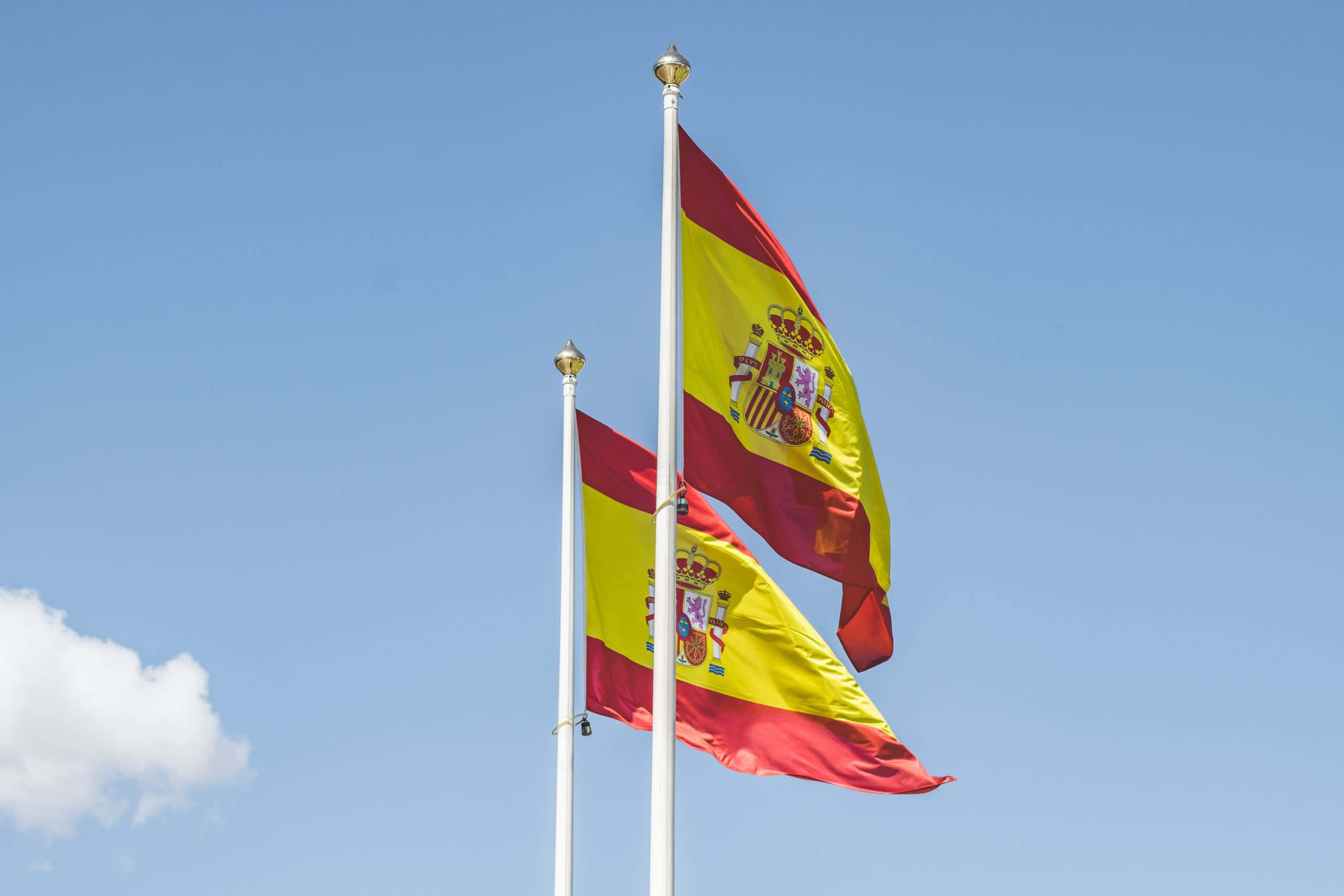 Flag 桌布 壁紙 — 兩面西班牙國旗在晴朗的藍天中自豪地飄揚，一朵白雲飄過。