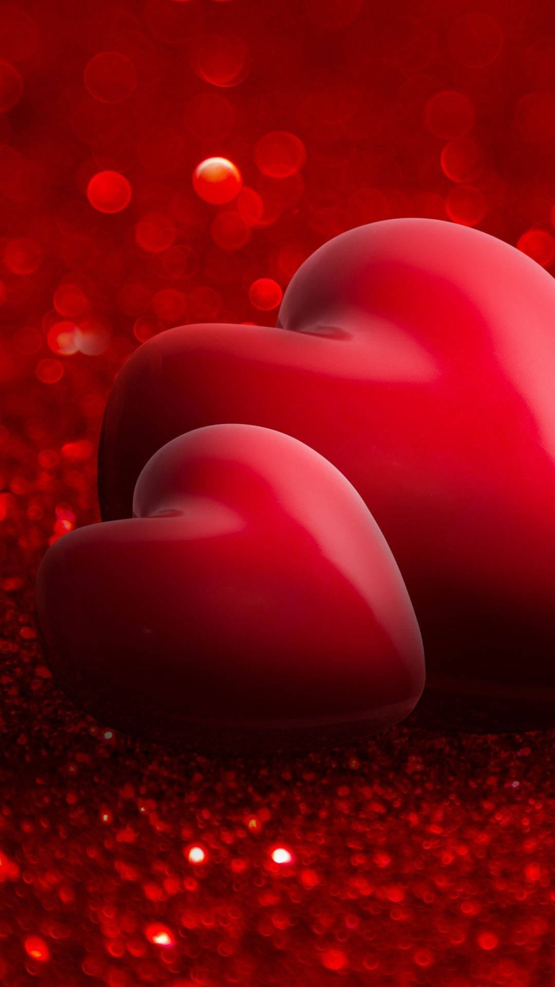 Love Phone 桌布 壁紙 — 兩顆光滑的紅色心形放在閃閃發光的紅色閃粉表面上，背景有散景燈光。