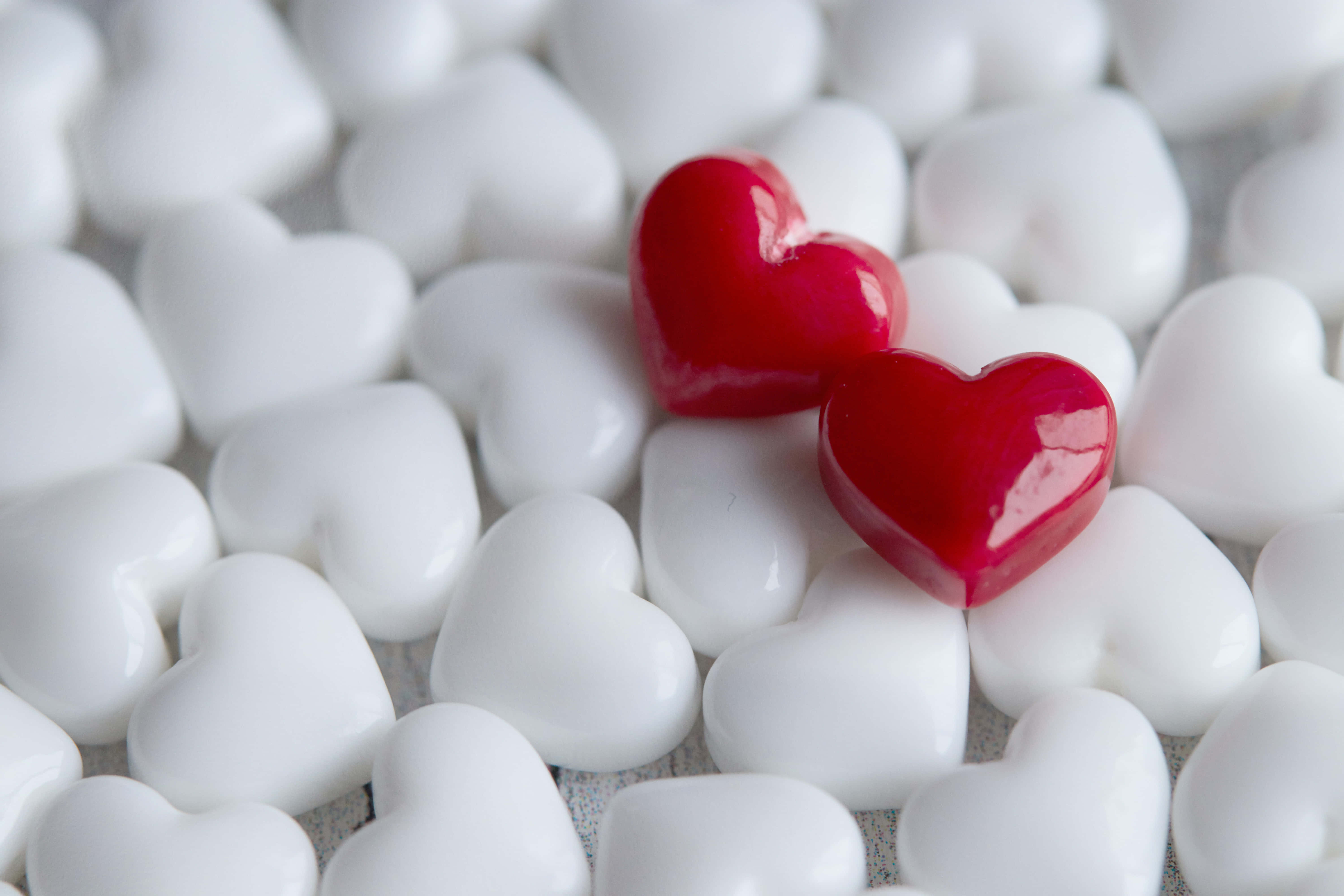 Cute Hearts 桌布 壁紙 — 兩顆光澤的紅色心形糖果放在一片白色心形糖果中，景深較淺。