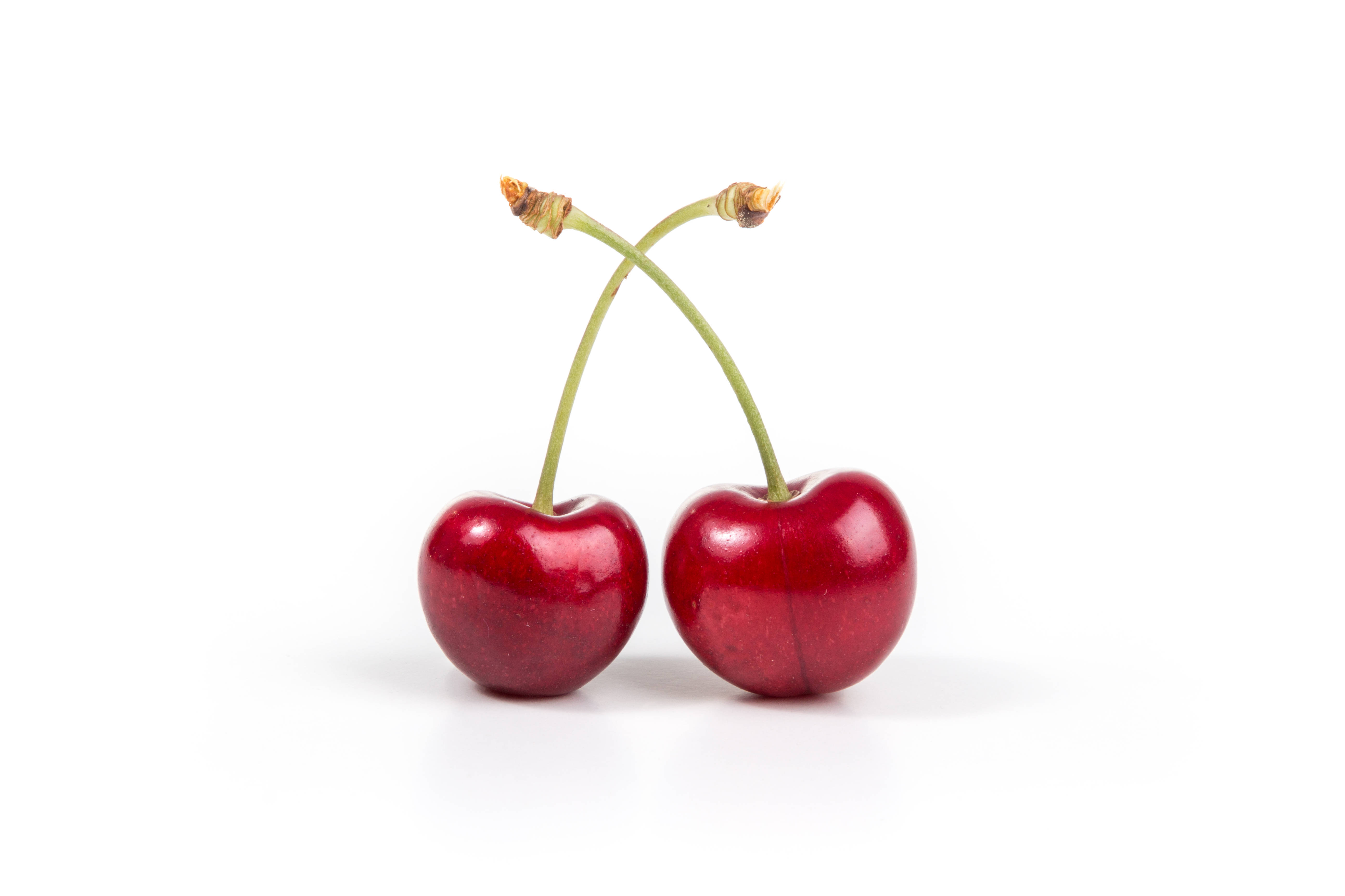 Cherry 桌布 壁紙 — 兩顆光澤的紅色櫻桃，帶有綠色莖，交叉在純白背景上。