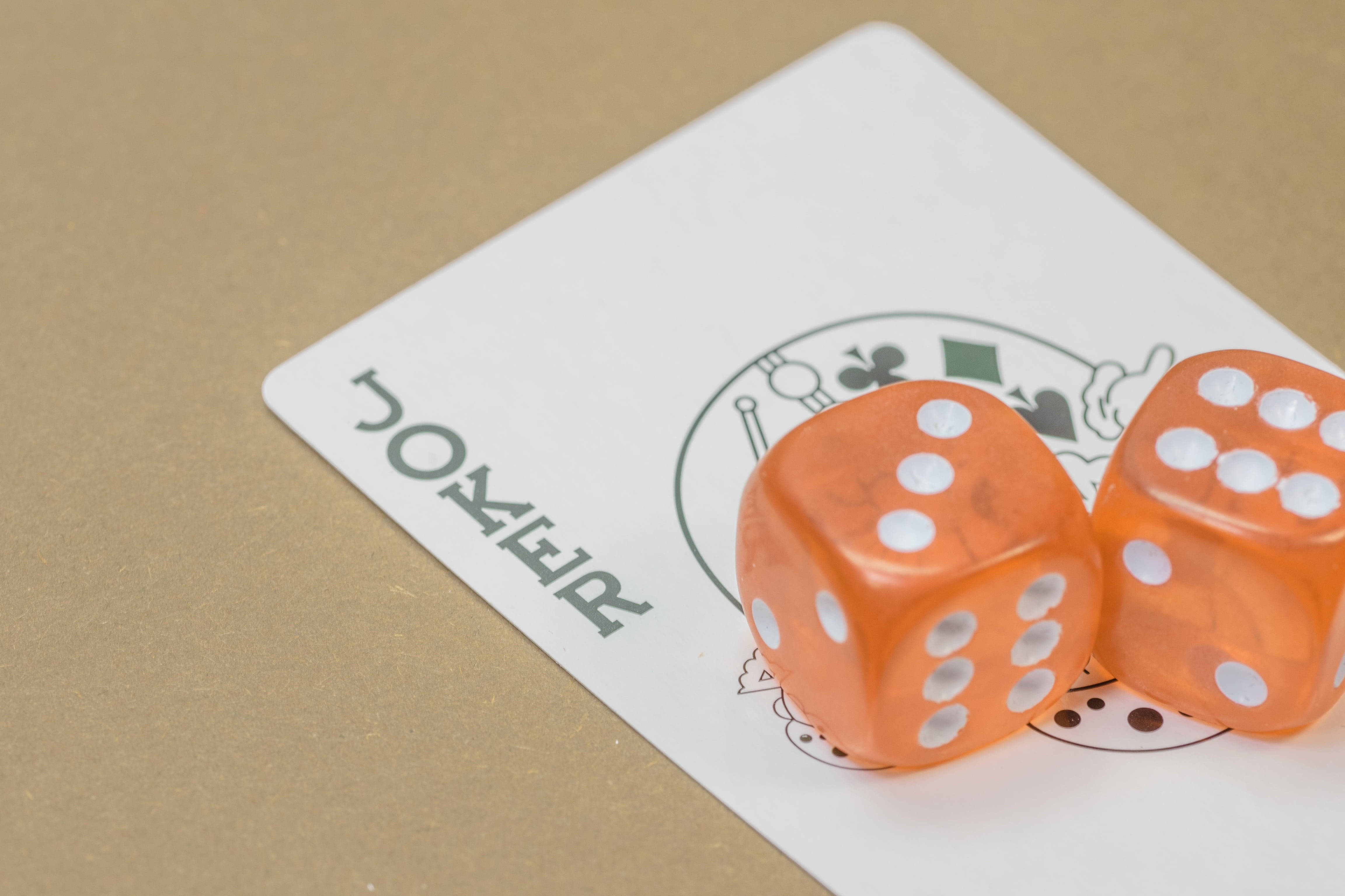 Dice 桌布 壁紙 — 兩顆半透明橙色骰子放在一張白色撲克牌上，牌上有卡通標誌，背景是棕色紙。
