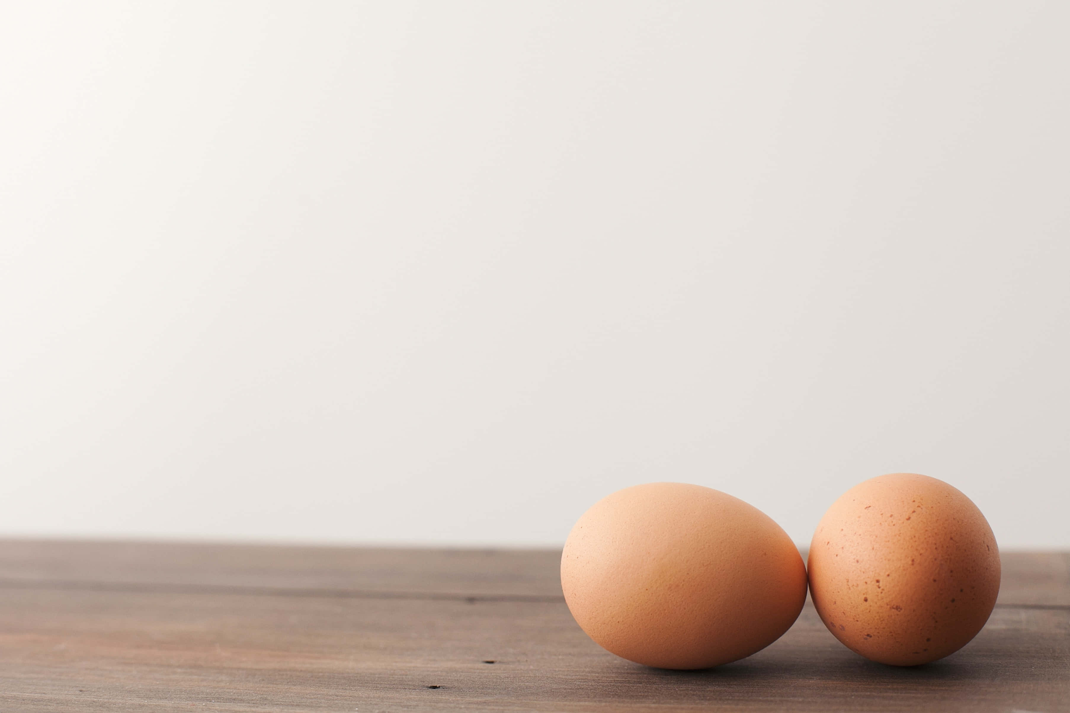 Egg 桌布 壁紙 — 兩顆棕色雞蛋並排放在木質表面上，背景為純白色。