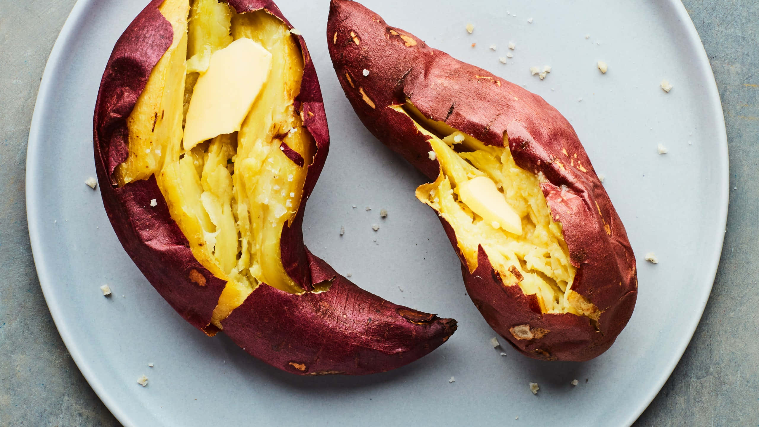 Yellow Sweet Potato 桌布 壁紙 — 兩顆烤地瓜在盤子上切開，露出蓬鬆黃色果肉，上面放有融化奶油和片狀鹽。